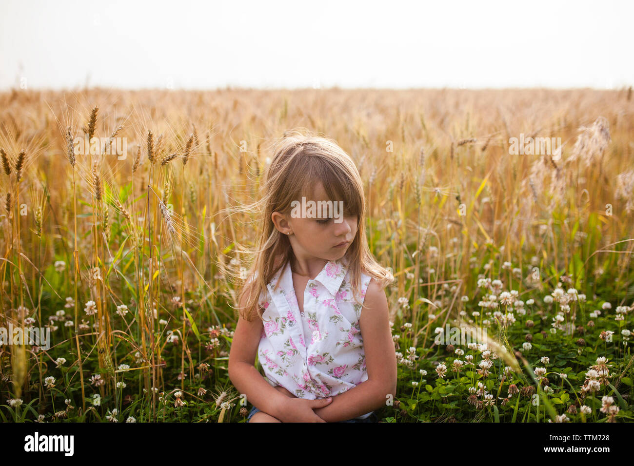 Verärgert Mädchen sitzen auf Feld gegen Himmel in Farm Stockfoto