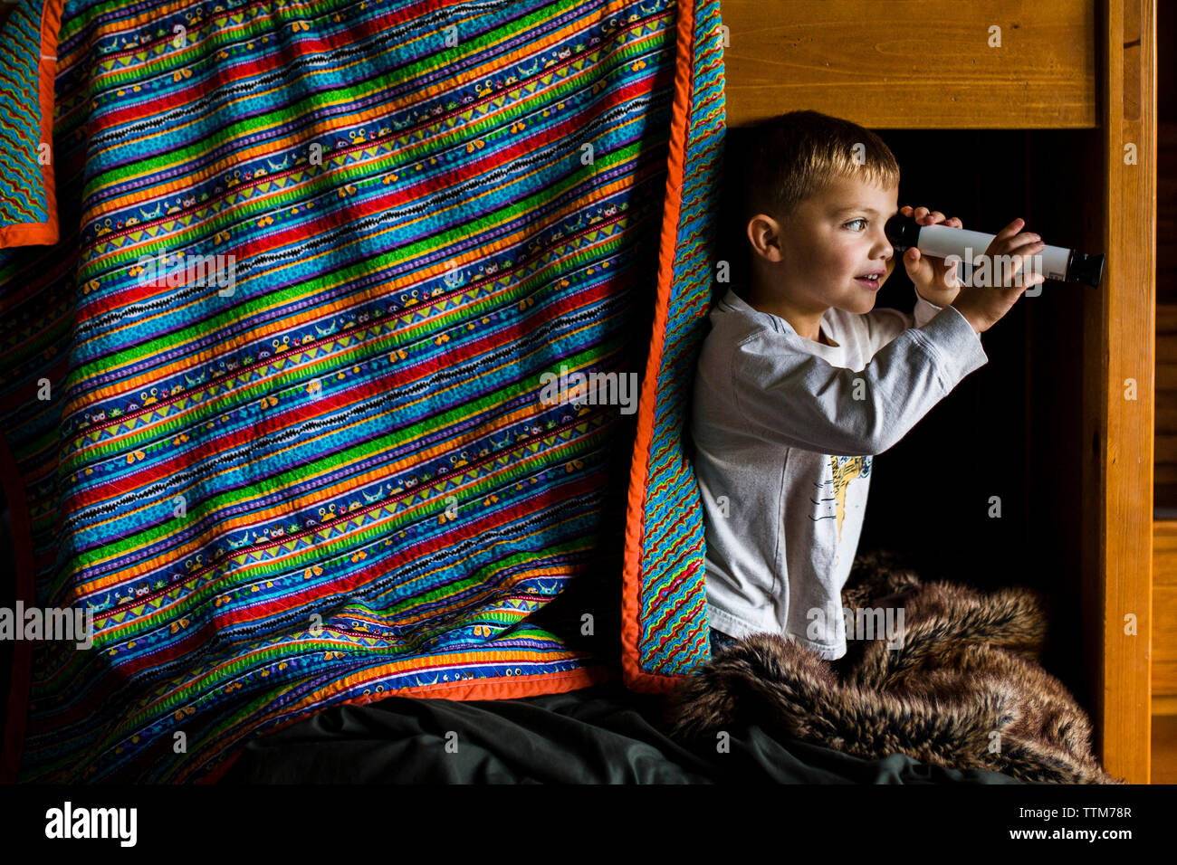 Neugierige junge Schauen durch Teleskop während auf ständigen Etagenbett Stockfoto