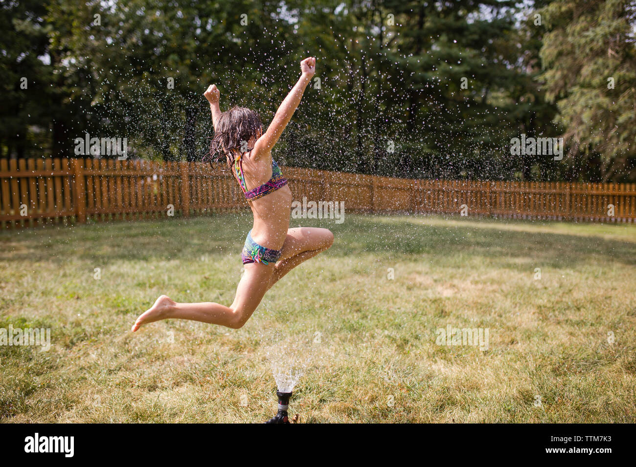 Fröhliches Mädchen über Sprinklerschutz im Hof springen Stockfoto