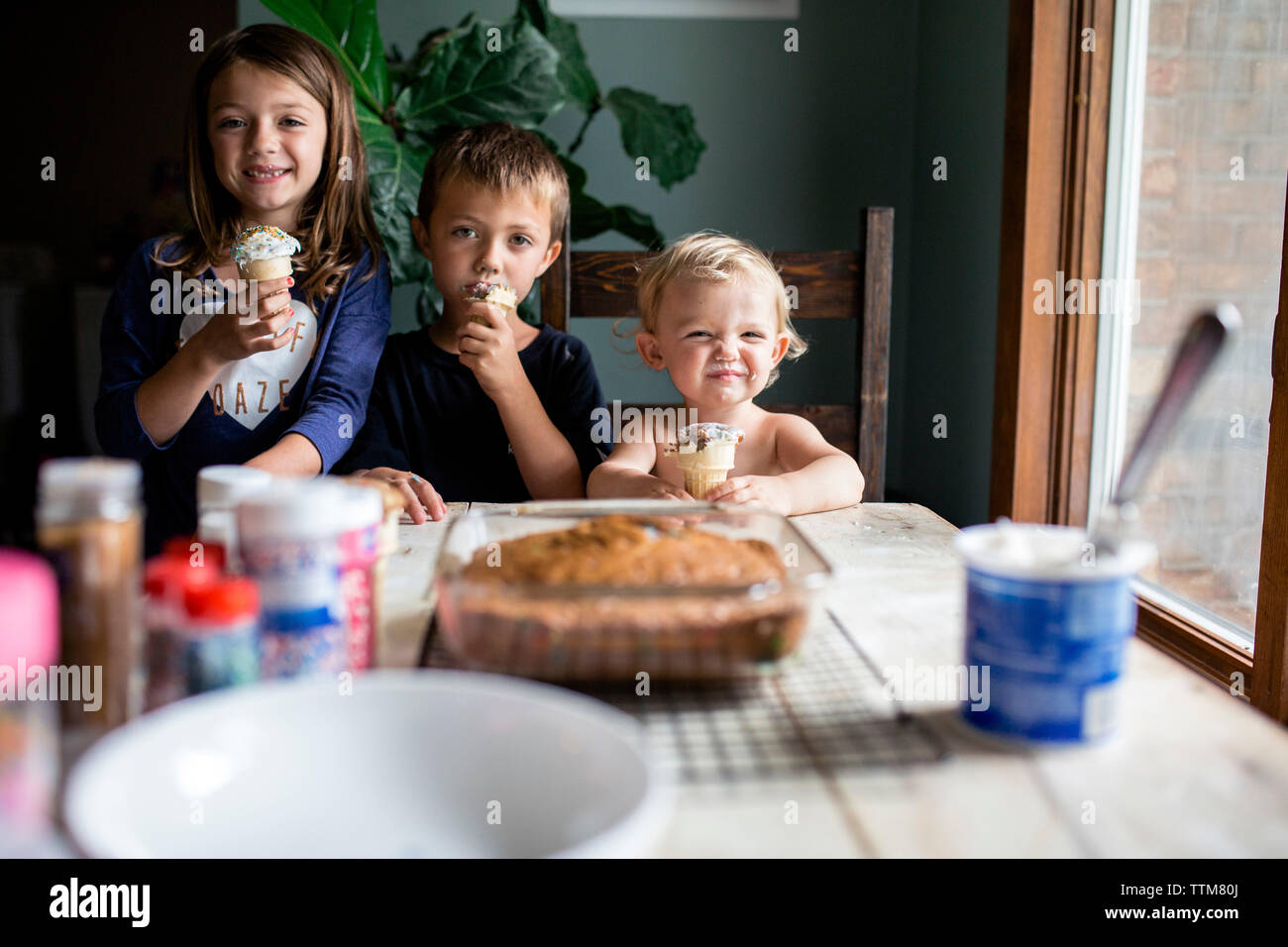 Drei junge Geschwister genießen Sie süße gebackene Leckereien im Innenbereich Stockfoto