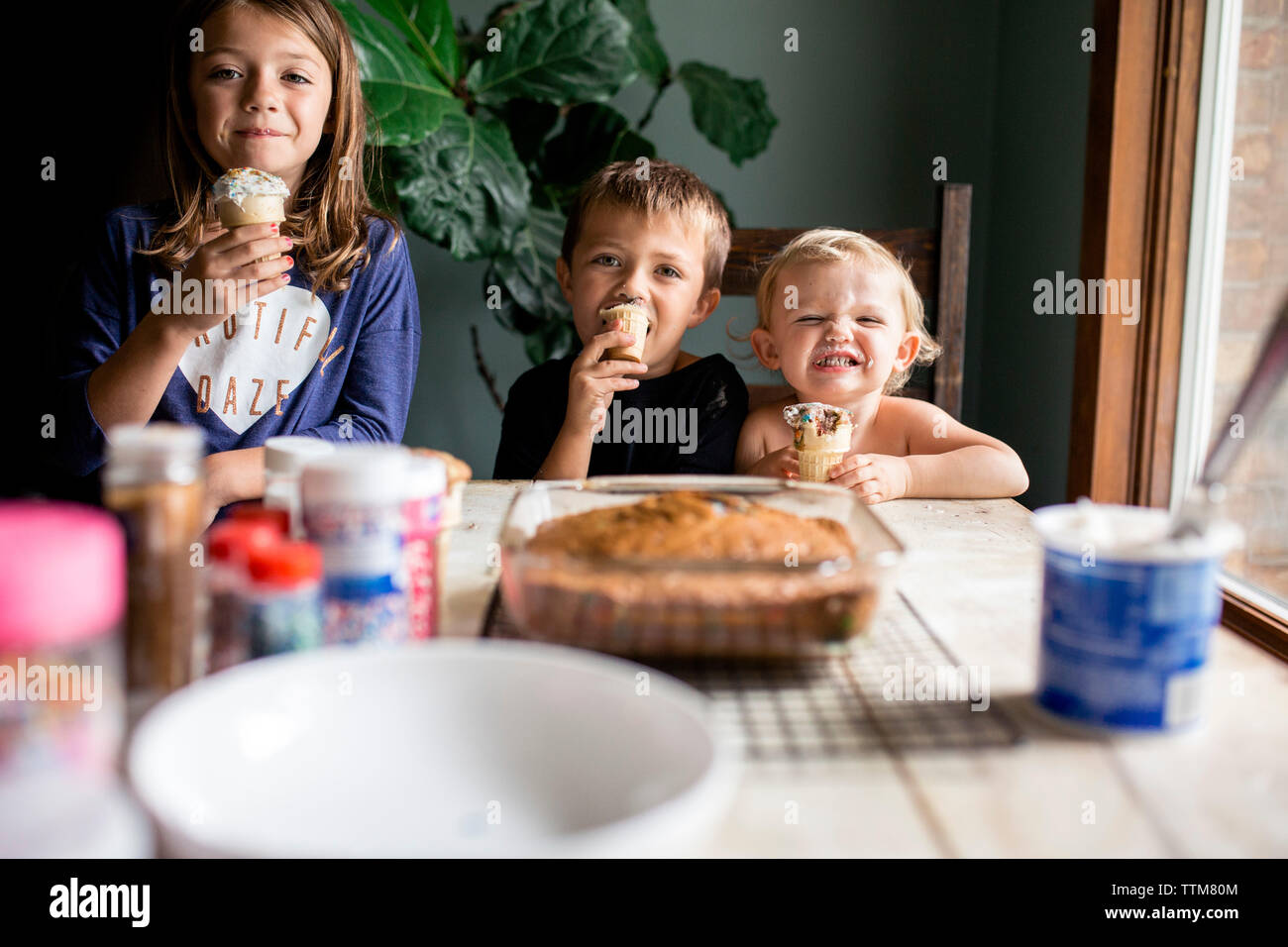 Drei junge Geschwister, goofy mit süßem Gebäck am Tisch Stockfoto