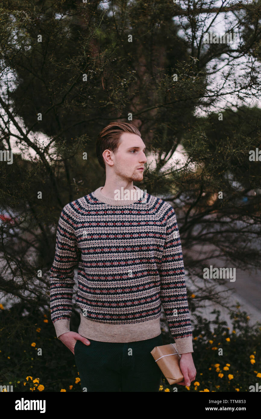 Nachdenklichen jungen Mann mit der Hand in der Tasche weg schauen gegen Pflanzen Stockfoto
