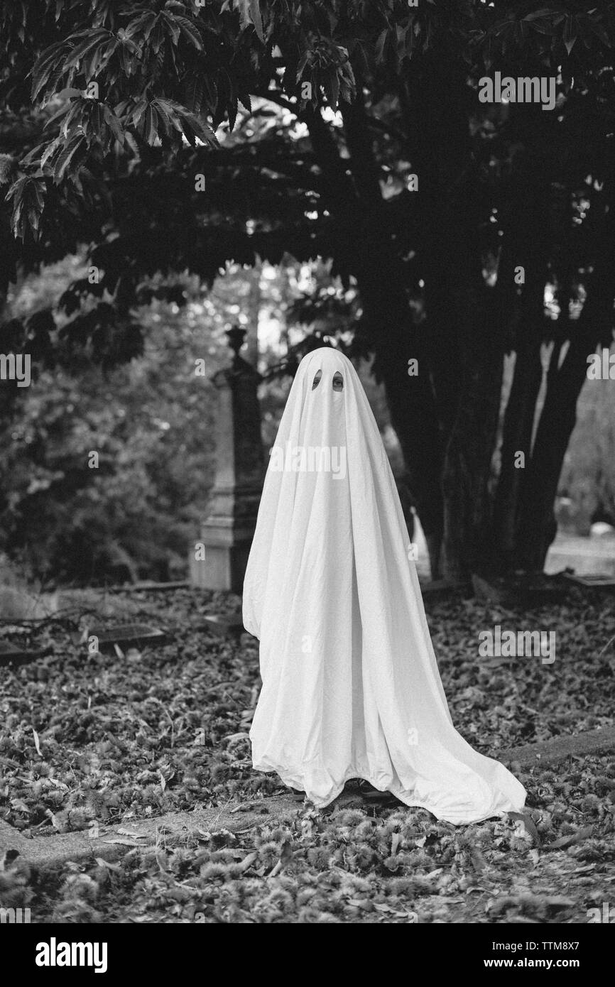 Porträt des jungen tragen ghost Kostüm beim Stehen auf Feld am Friedhof während der Halloween Stockfoto