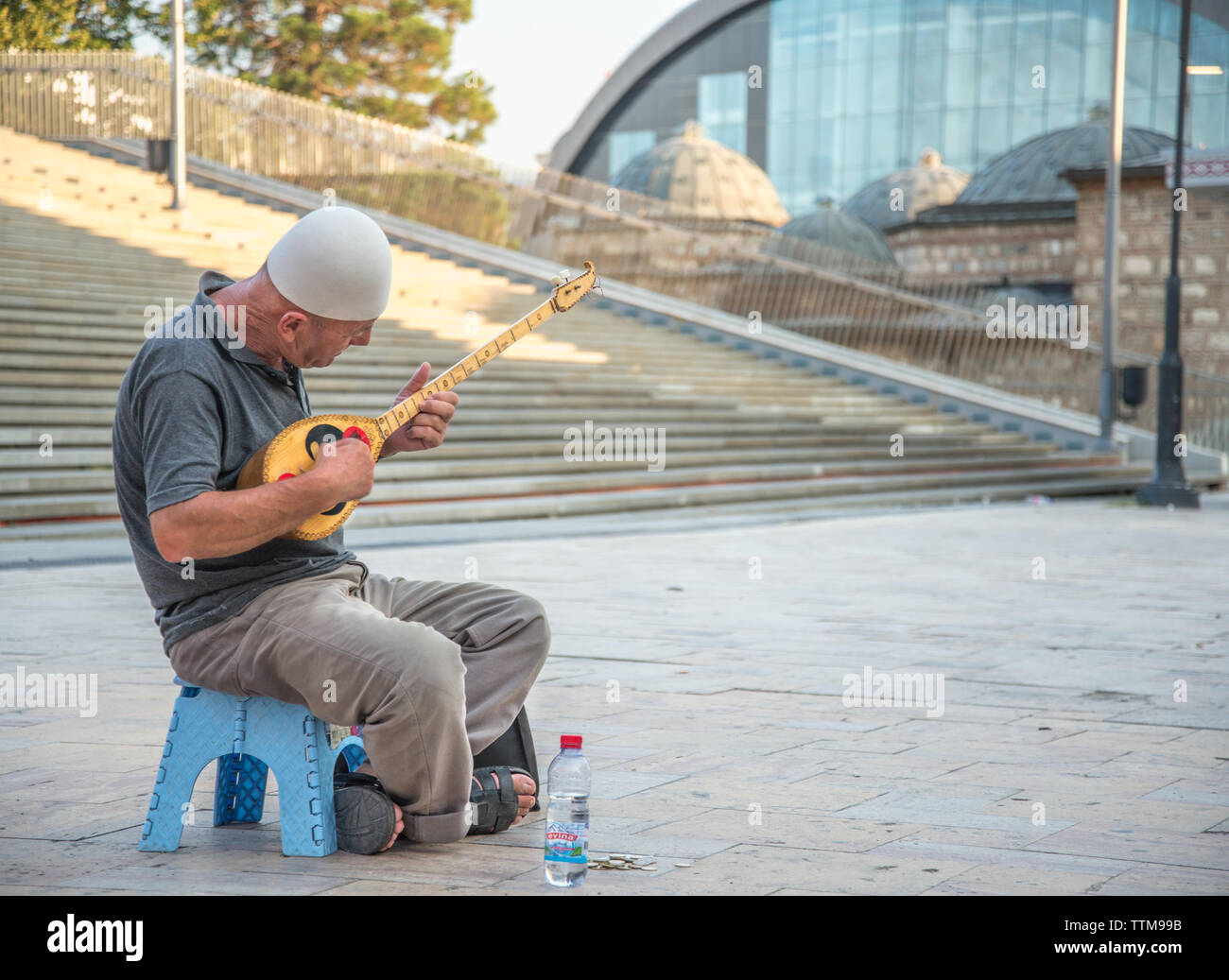 Älterer Mann spielt Musik auf einem massivem Messing Saiteninstrument, ausserhalb in den alten Basar von Skopje sitzen. Stockfoto