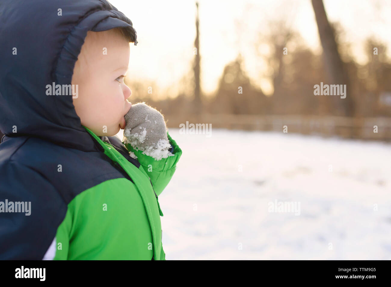 Junge mit Finger im Mund weg schauen, während man im Hinterhof im Winter Stockfoto