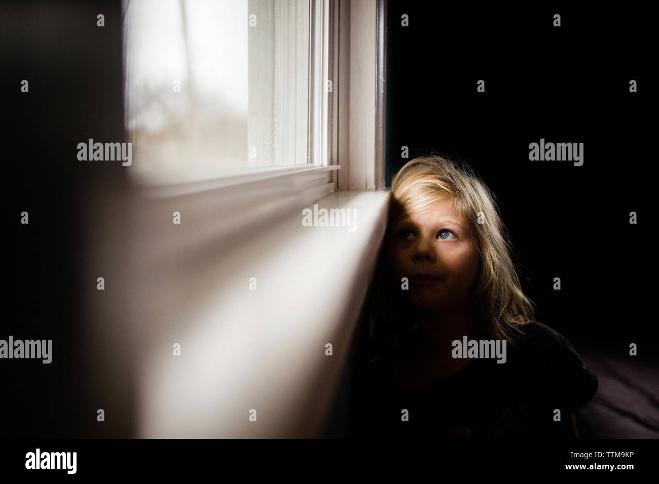 Nachdenkliches Mädchen Blick durch Fenster, während zu Hause sitzen Stockfoto