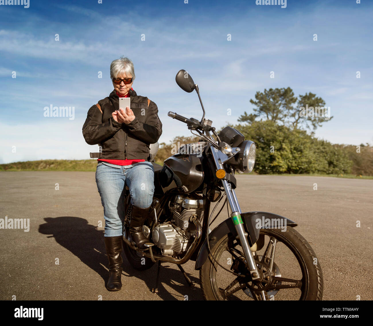 Ältere Frau mit Smart Phone, während mit dem Motorrad auf der Straße Stockfoto