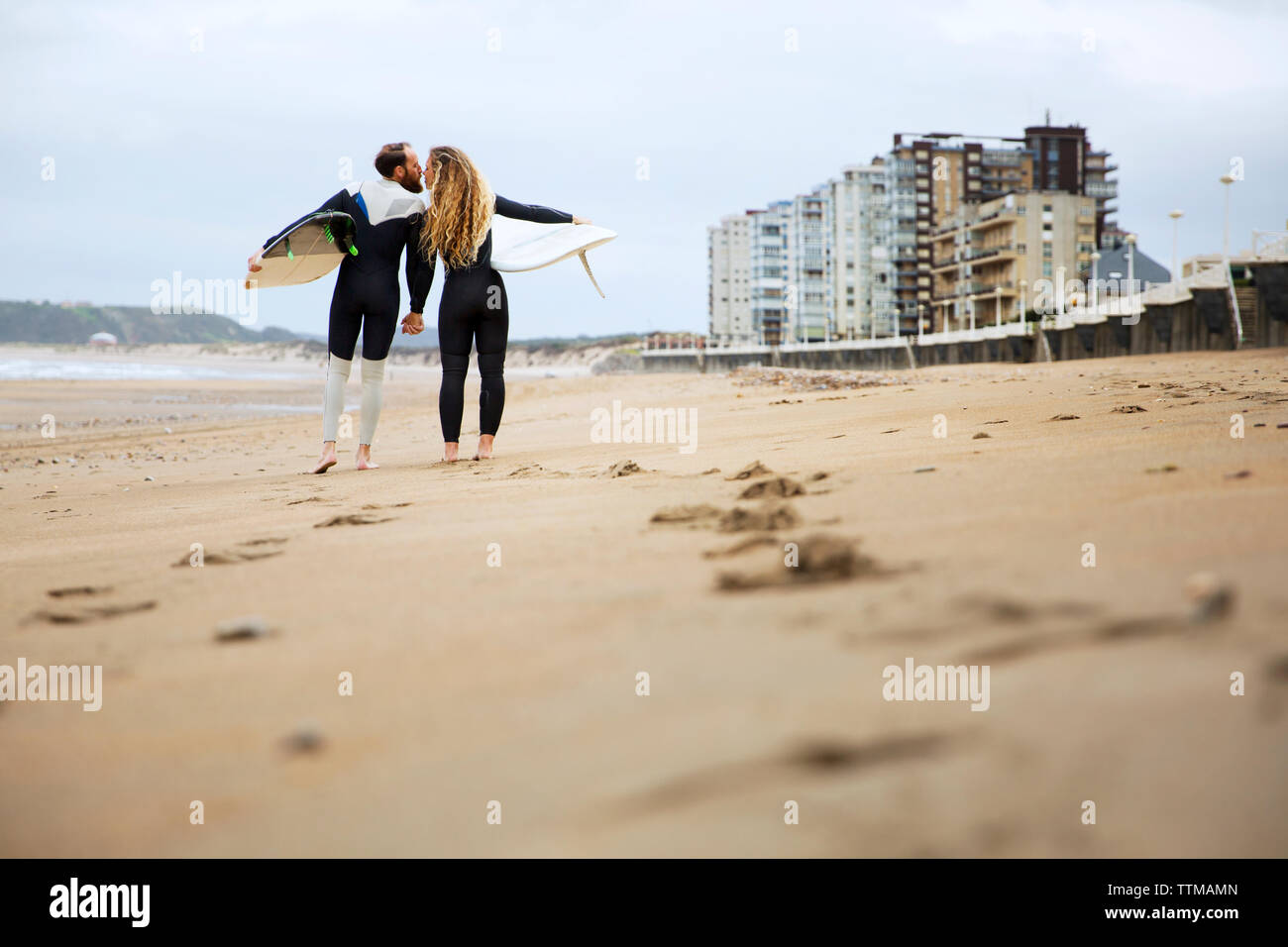 Paar küssen, während Sie surfbretter am Strand Stockfoto