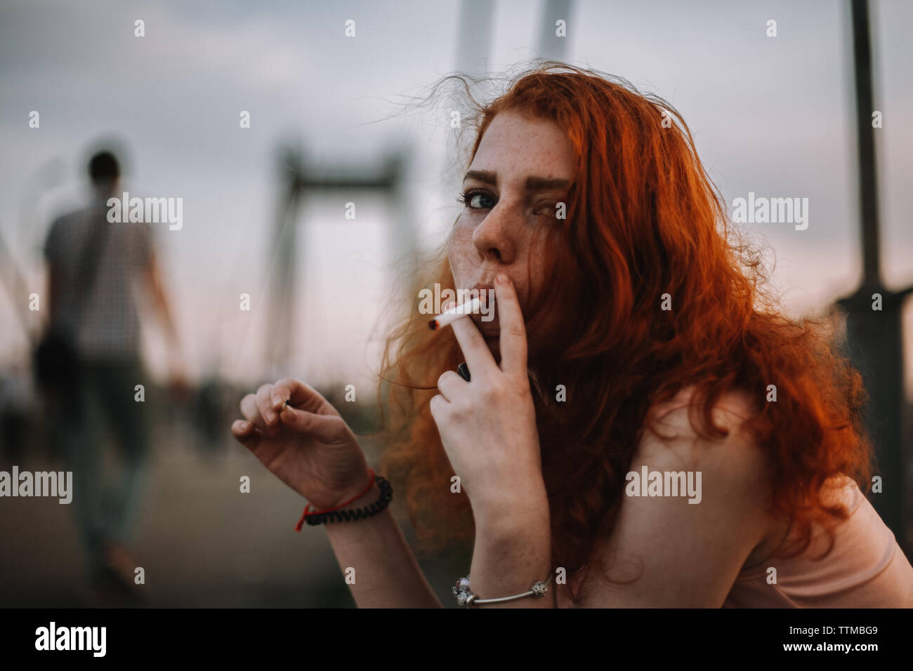 Junge rothaarige Frau rauchen Zigarette sitzen auf der Brücke in der Stadt Stockfoto