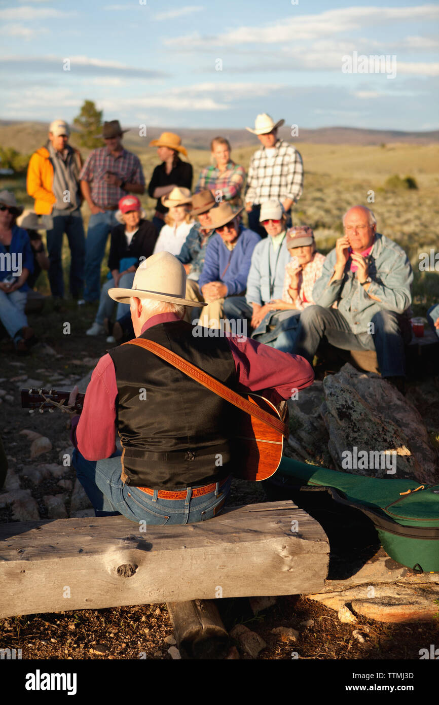 USA, Wyoming, Lager, Gäste an einem Dude Ranch Sitzen am Lagerfeuer und ein Mann Gitarre spielen hören und Country Western Songs singen, Abara Ranch Stockfoto