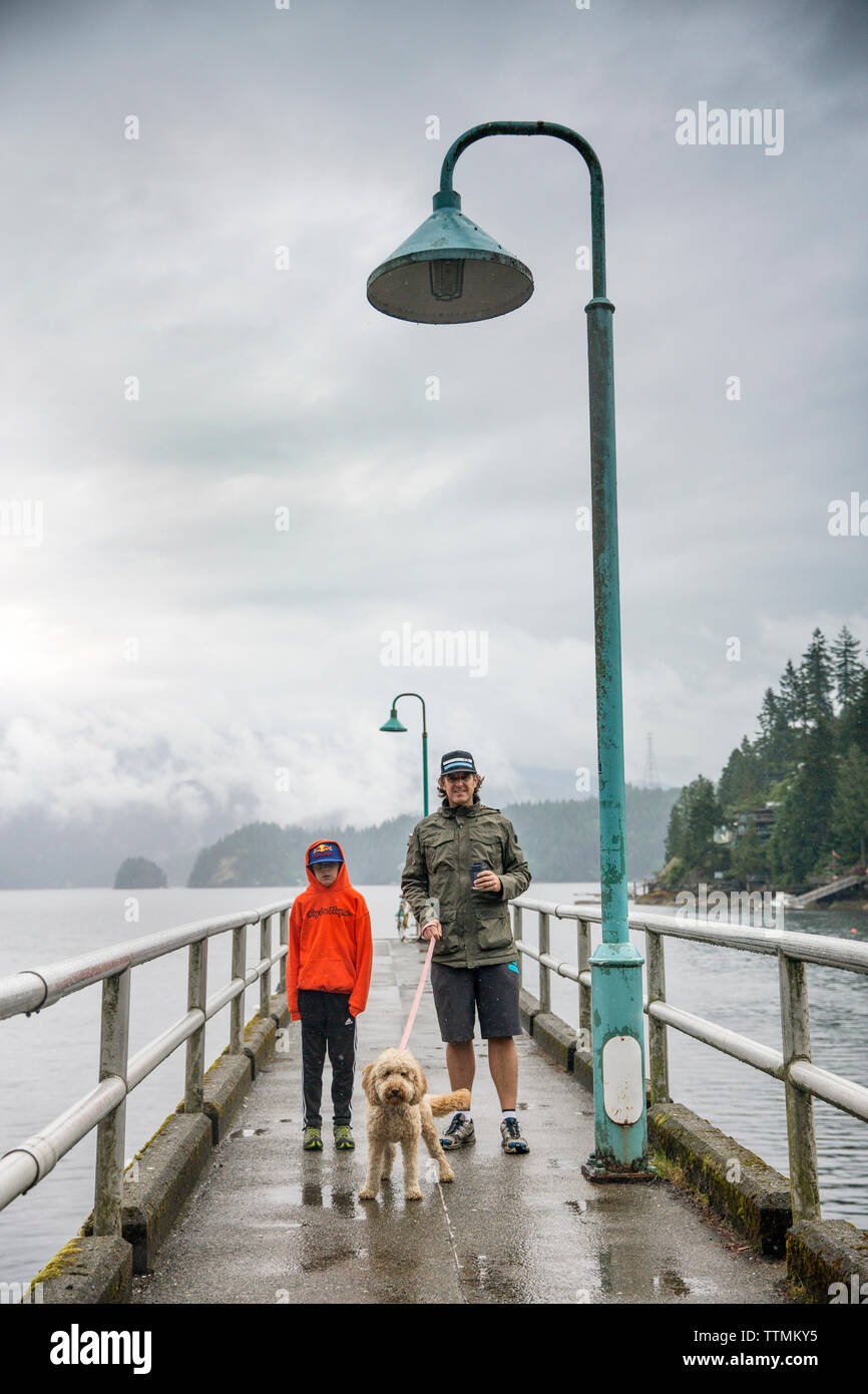 Kanada, Vancouver, British Columbia, Vater und Sohn stehen mit ihrem Hund auf dem Pier in Deep Cove, North Vancouver Stockfoto