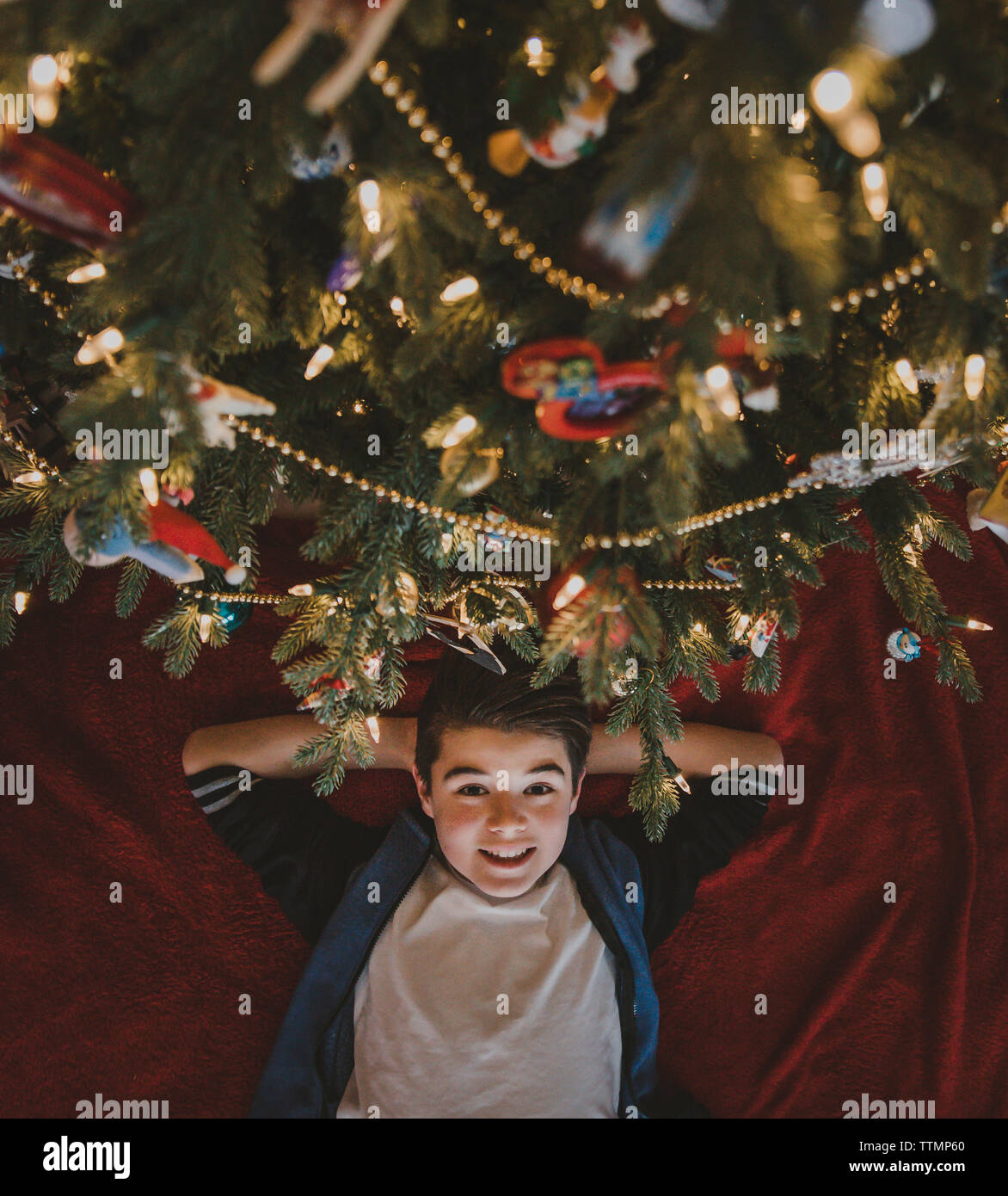 Kopfporträt eines Jungen mit Händen hinter Kopf, der zu Hause am weihnachtsbaum liegt Stockfoto