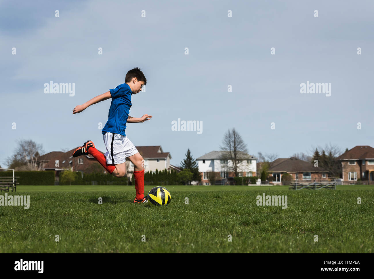 Seitenansicht des Jungen kicken Fußball beim Spielen auf der Wiese Stockfoto