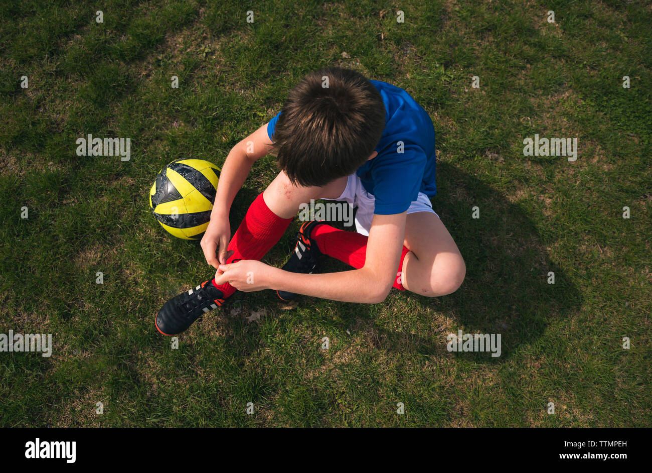 Hohe Betrachtungswinkel von boy Schnürsenkel binden beim Sitzen auf Fußball-Feld Stockfoto