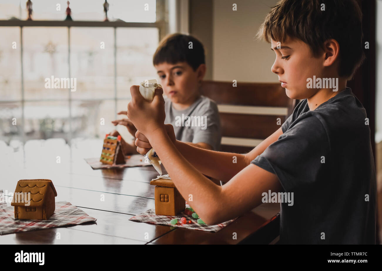 Zwei Jungen dekorieren Lebkuchenhäuser zusammen am Tisch. Stockfoto