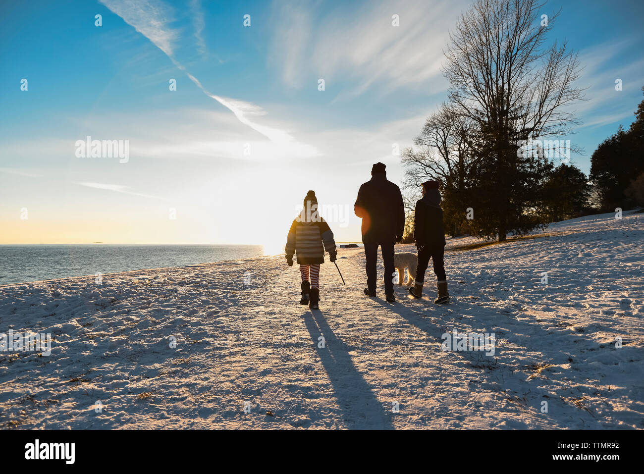 Silhouette von Familie wandern auf einem verschneiten Weg bei Sonnenuntergang. Stockfoto