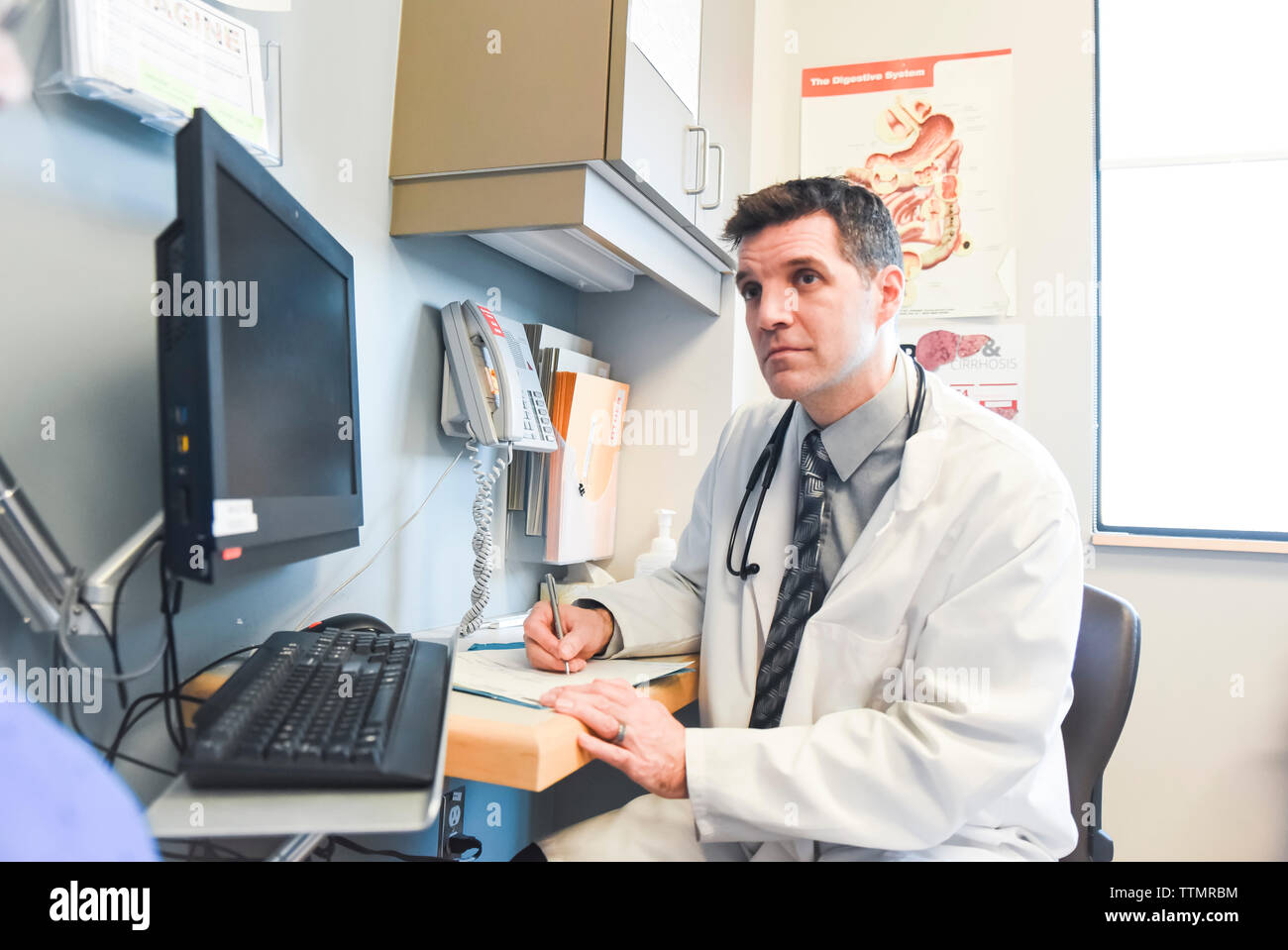 Arzt hört geduldig zu und Schreiben an einem Schreibtisch in einer Klinik. Stockfoto