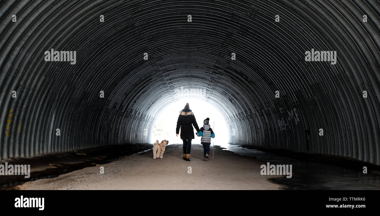 Mutter, Sohn und Hund gehen durch einen Tunnel aus Metall an einem Wintertag. Stockfoto