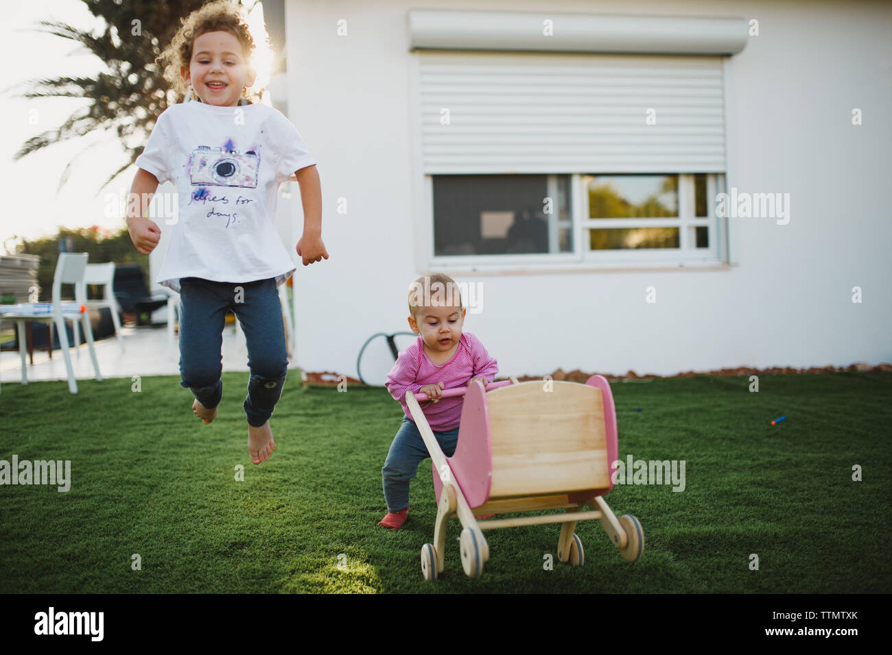 Zwei Schwestern, die zusammen spielen im Hof springen mit doll Stroller Stockfoto