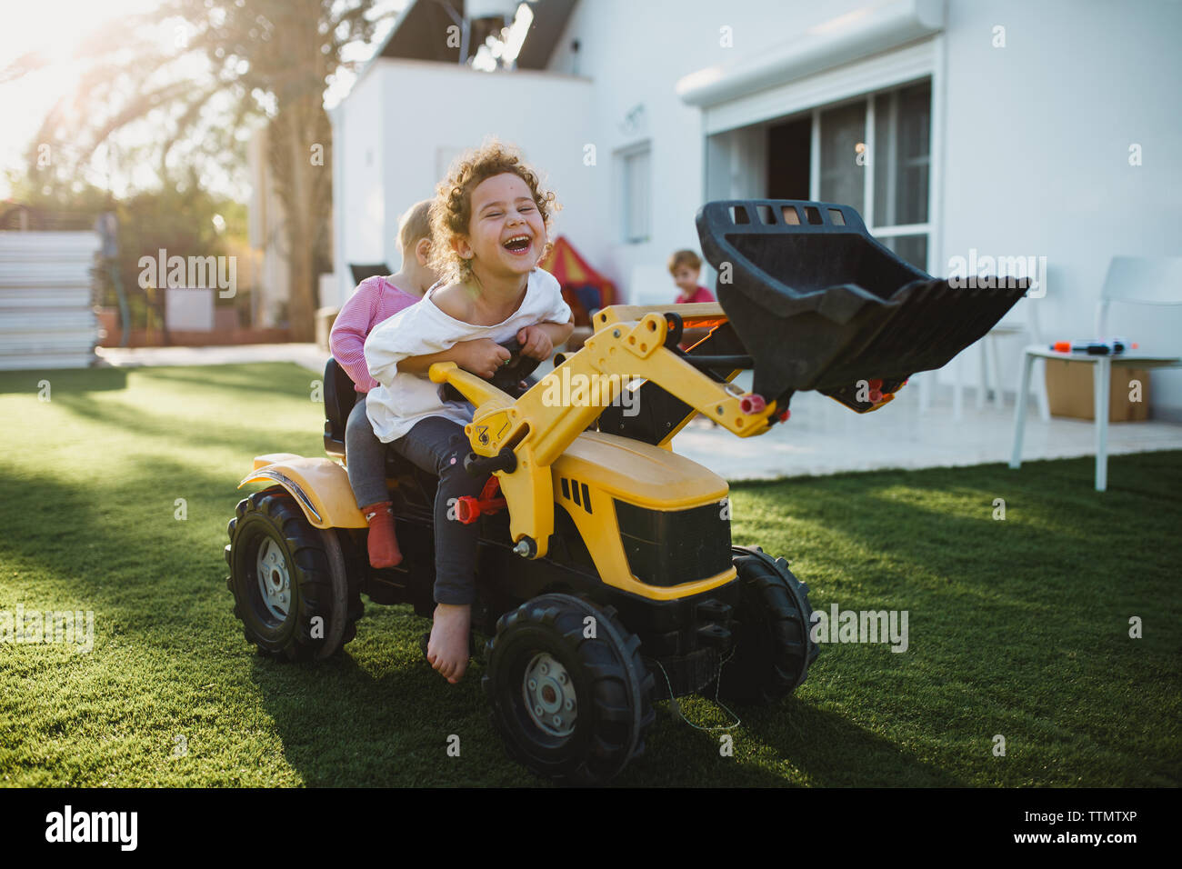 Ein junges Mädchen lachend, während auf ein Spielzeug Traktor draußen im Hof sitzen Stockfoto