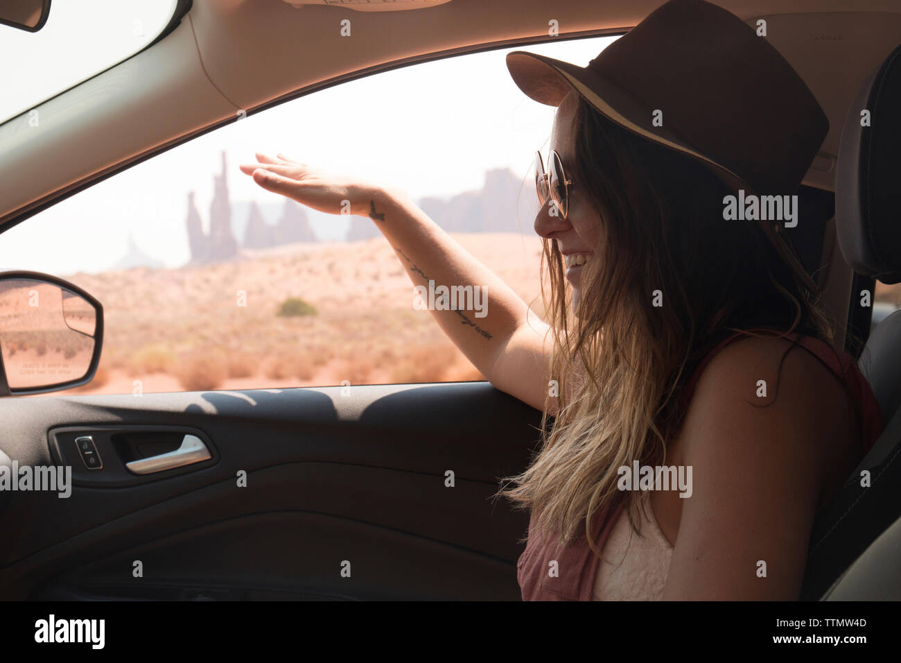Seitenansicht der lächelnde Frau mit Hut und Sonnenbrille beim Sitzen im Auto am Monument Valley Tribal Park Stockfoto