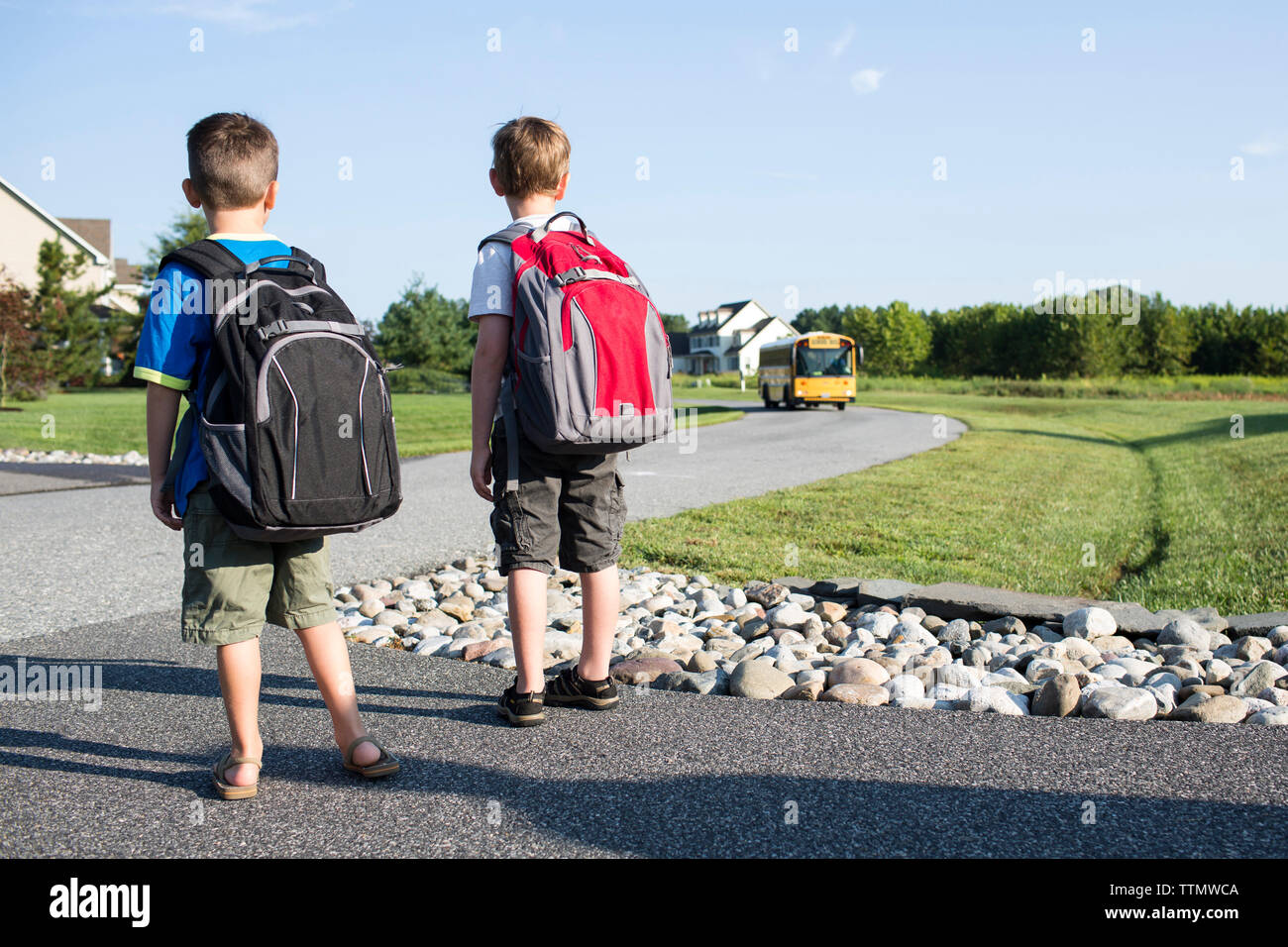 Rückansicht der Schüler warten auf School Bus auf der Straße gegen Sky Stockfoto