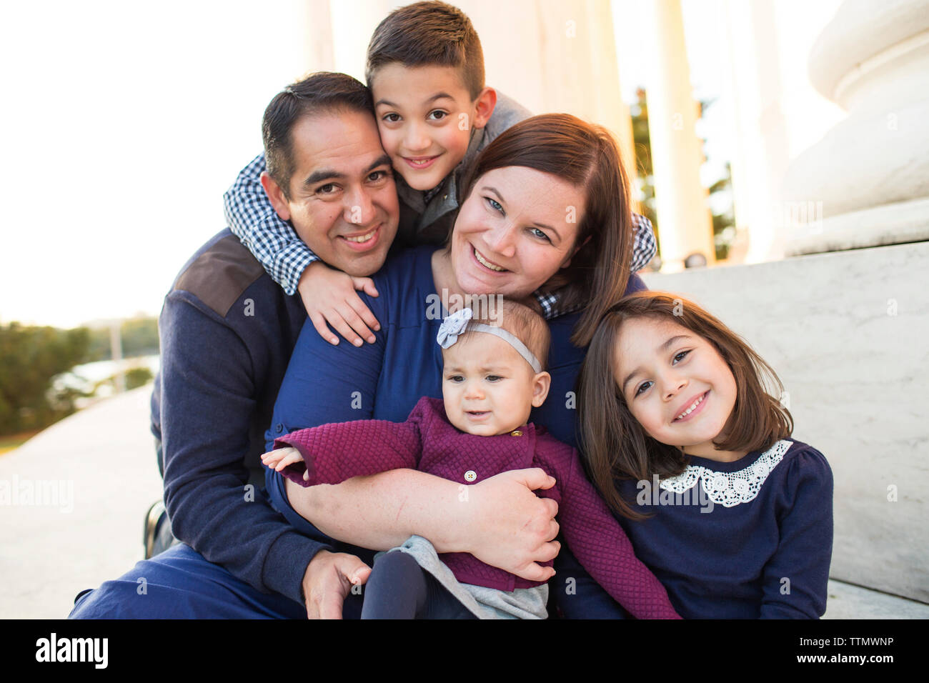 Portrait von glücklichen Eltern mit Kindern sitzen auf stützmauer im Park bei Sonnenuntergang Stockfoto