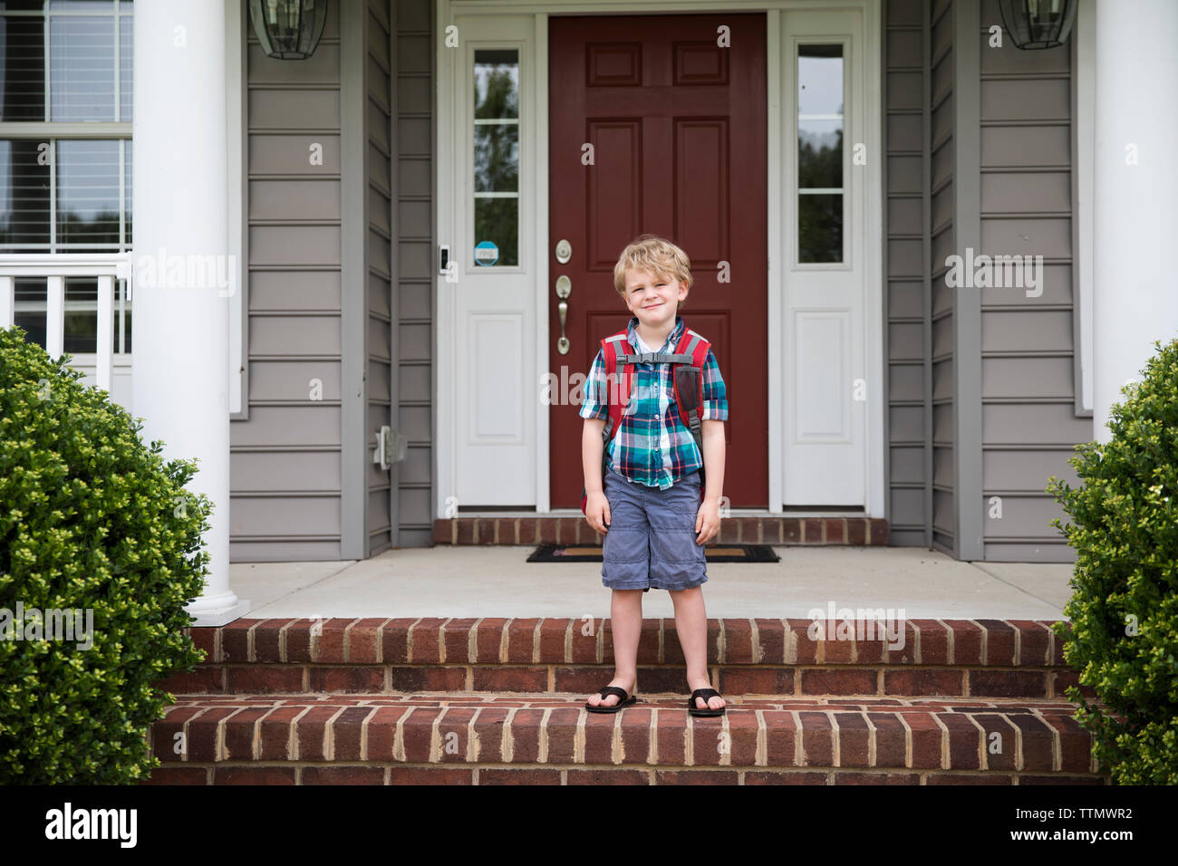 Süße blonde lockige vorangegangen Boy wartet auf Schulbus auf vorderen Stufen Stockfoto