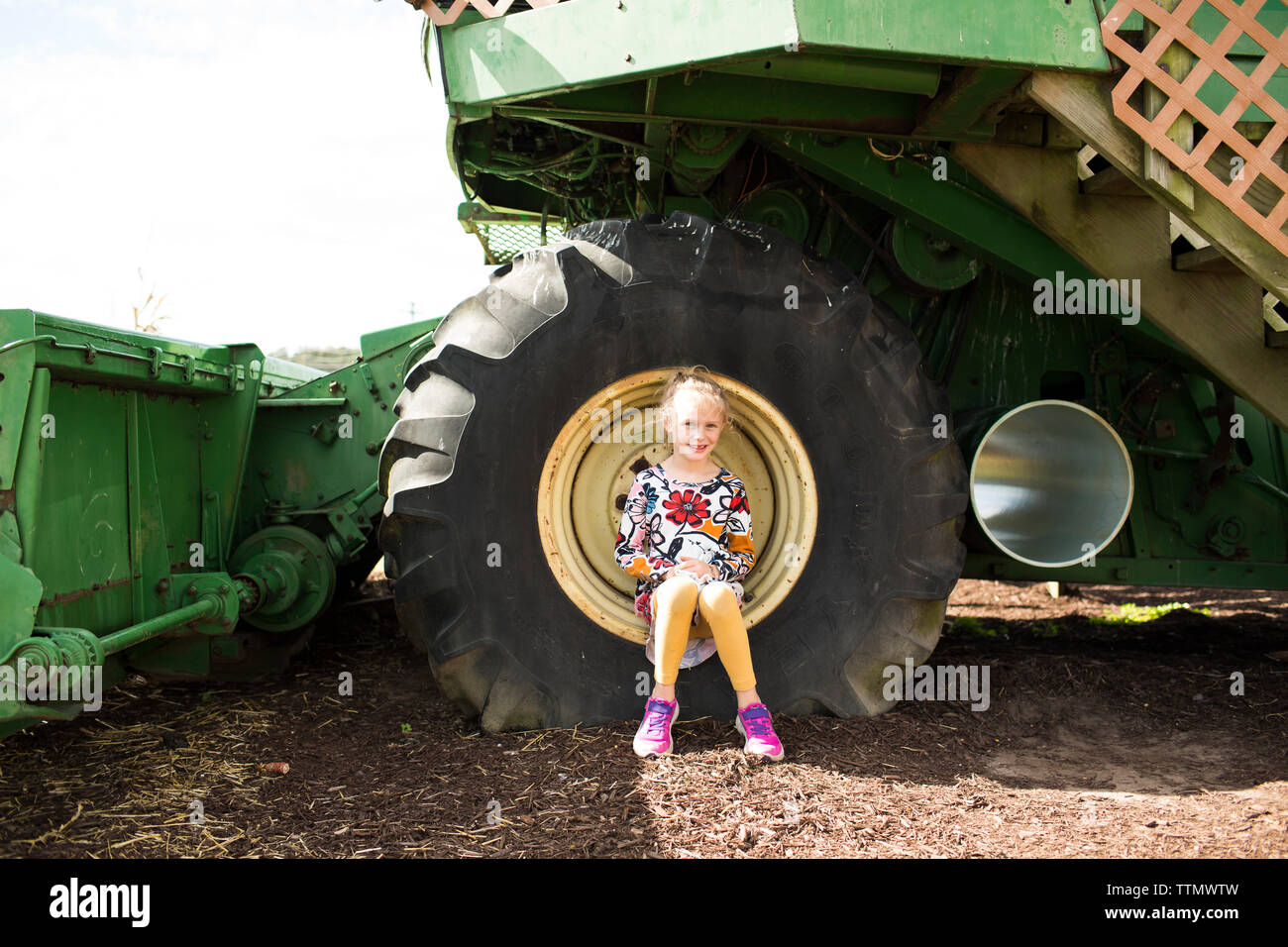Süße blonde Mädchen in bunten Kleid Sitzen in landwirtschaftlichen Geräten Reifen Stockfoto