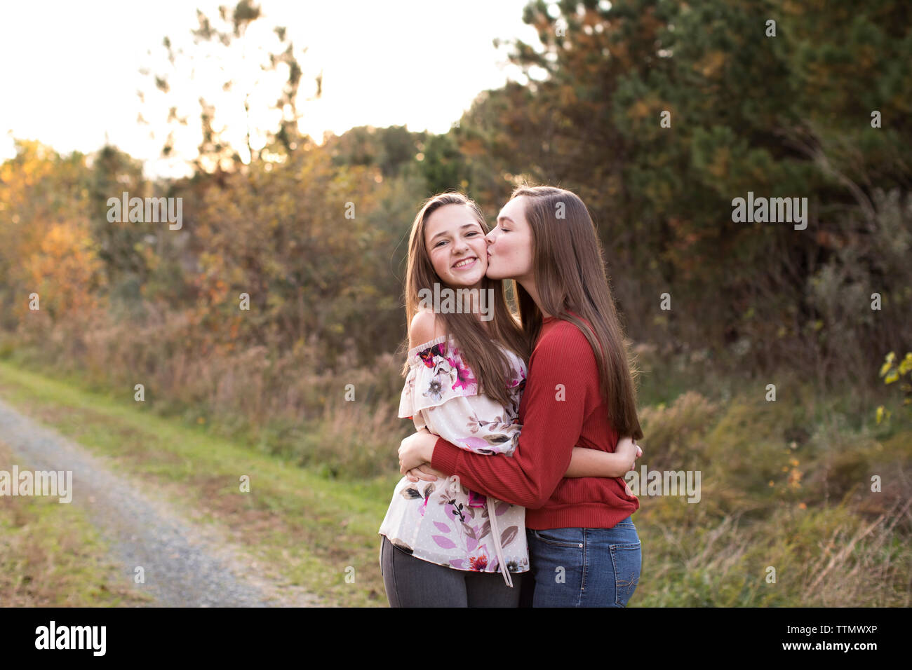 Jugendlich Mädchen küsse Teen Schwester auf die Wange auf einem Trail bei Sonnenuntergang im Herbst Stockfoto