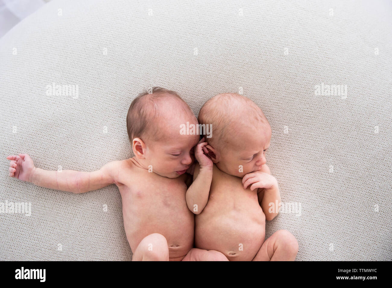 Neugeborene Zwillinge mit Armen und Beinen verflochten Verlegung auf weiße Decke Stockfoto