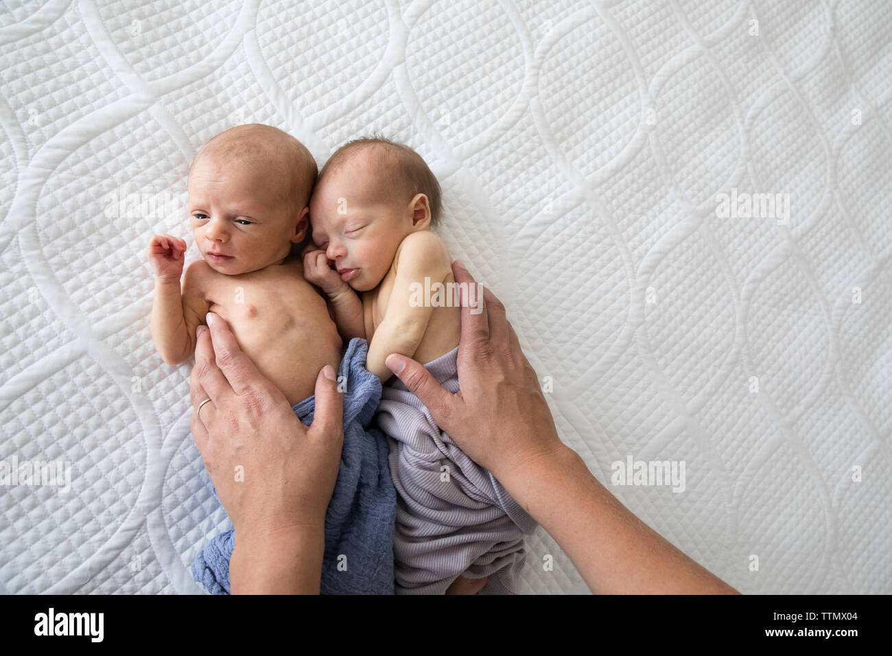Die Gemeinkosten der Neugeborenen zwei Mädchen auf dem Bett und wurde von der Mutter getröstet Hände Stockfoto