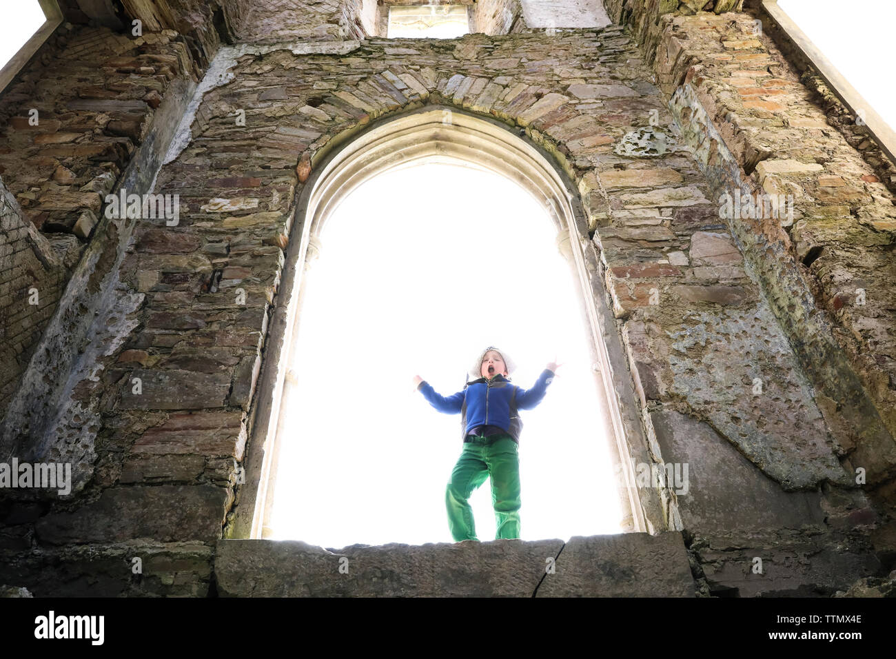 Junge macht dumm Stellen beim Stehen in der großen steinernen Burg Fenster Stockfoto