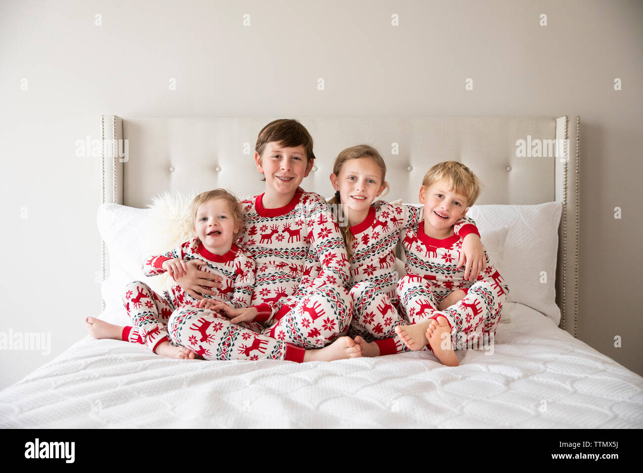 Vier Kleinkind zu Tween Geschwister in Urlaub Schlafanzug Umarmen auf weißen Bett Stockfoto