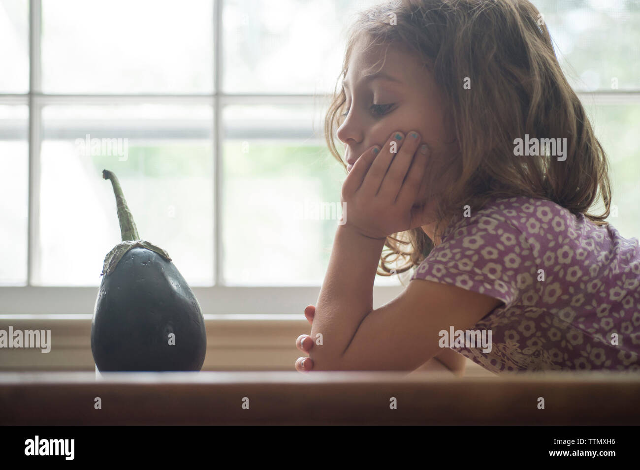 Gelangweilt Mädchen auf Auberginen durch Fenster in Home Stockfoto
