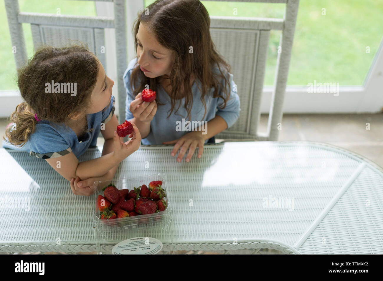 Hohe Betrachtungswinkel der Schwestern Gesicht zu beim essen Erdbeeren am Tisch Gesicht Stockfoto