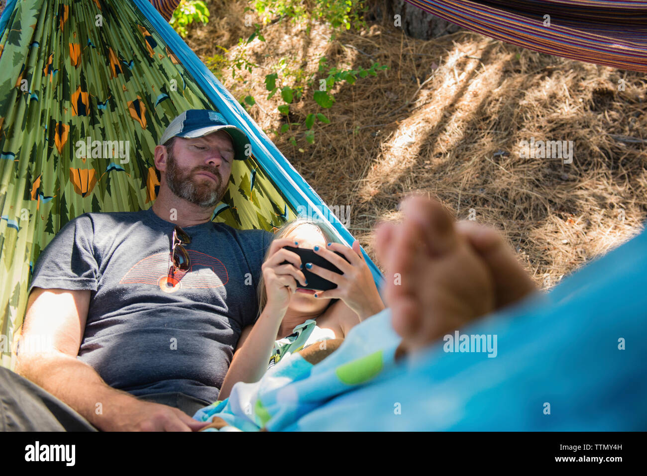 Hohe Betrachtungswinkel der Tochter mit Smart Phone beim Lügen mit Vater in der Hängematte am Wald Stockfoto