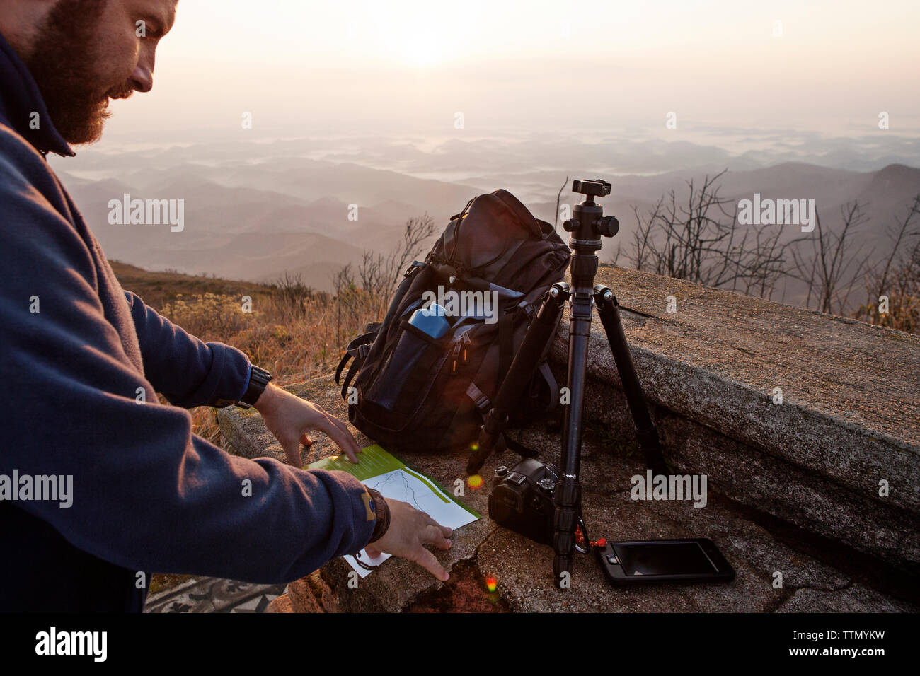 Mann Lesung auf Karte beim Stehen auf die Berge bei Sonnenuntergang Stockfoto