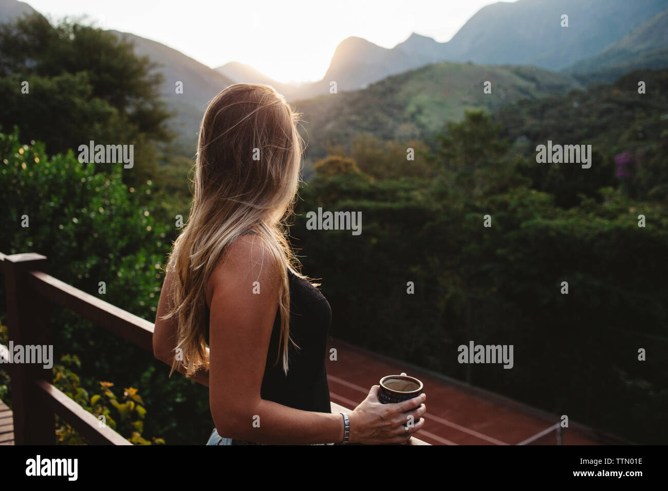Seitenansicht der Frau mit Kaffee Tasse durch Geländer gegen Bergen stehend Stockfoto