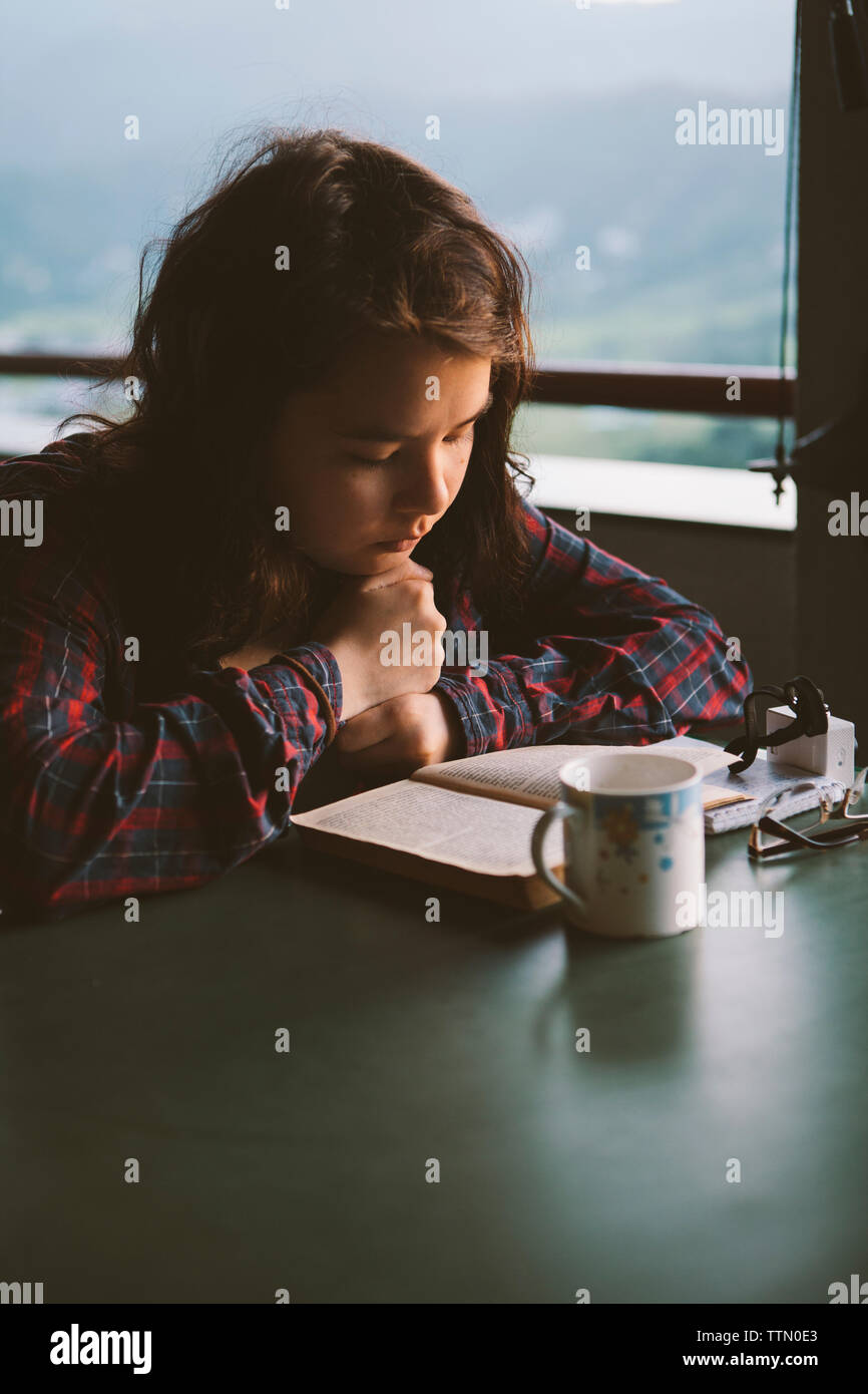 Junge Frau mit Buch mit Tasse Kaffee am Tisch Stockfoto