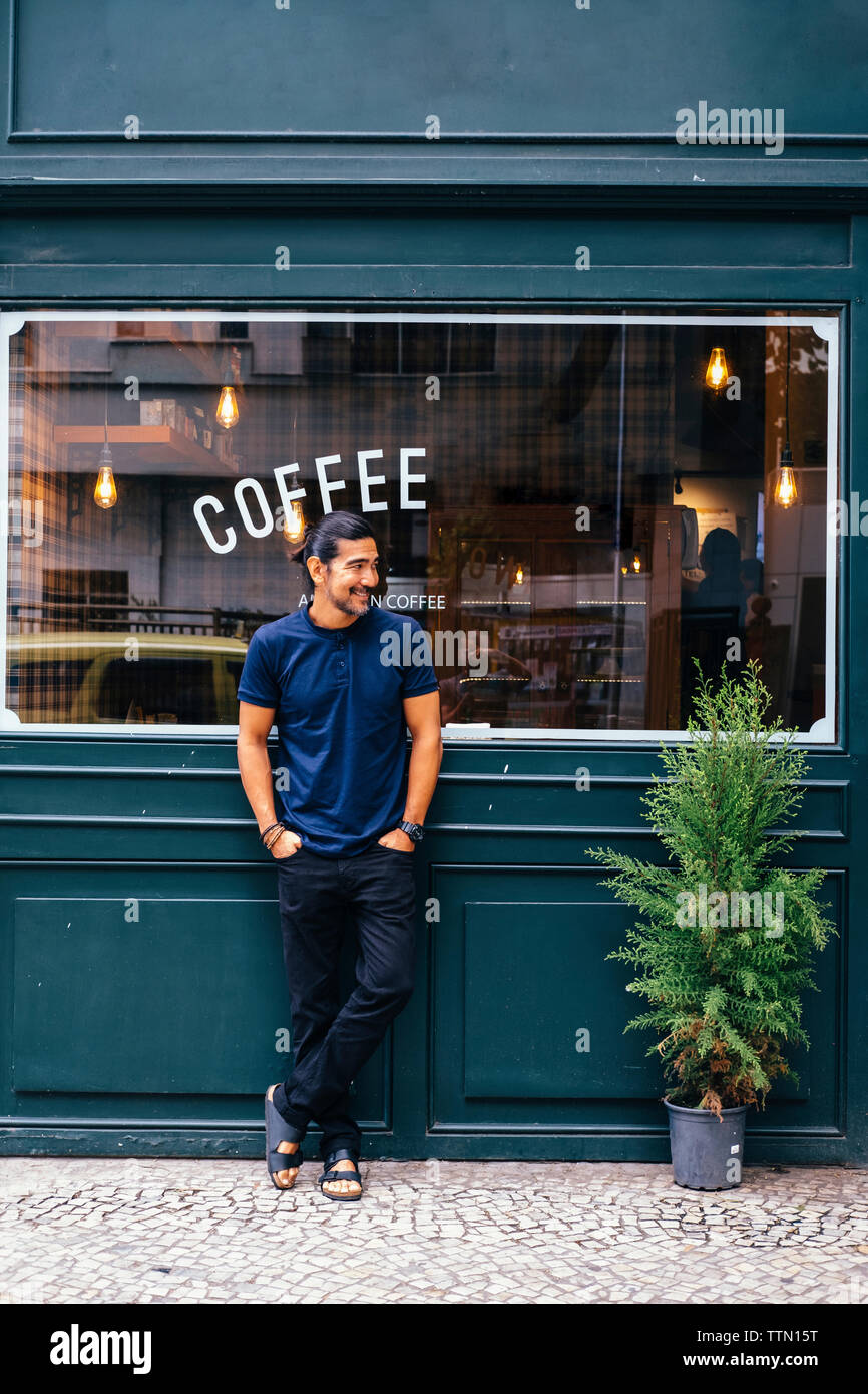 Volle Länge des lächelnden reifer Mann mit Händen in den Taschen gegen Coffee Shop Stand Stockfoto