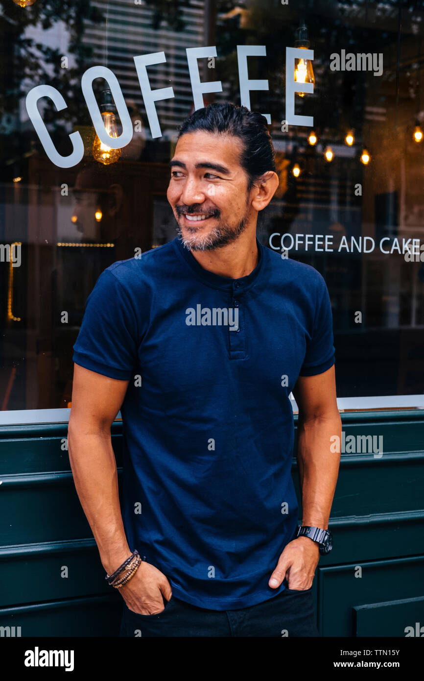 Lächelnd reifer Mann mit Händen in den Taschen gegen Coffee Shop Stand Stockfoto