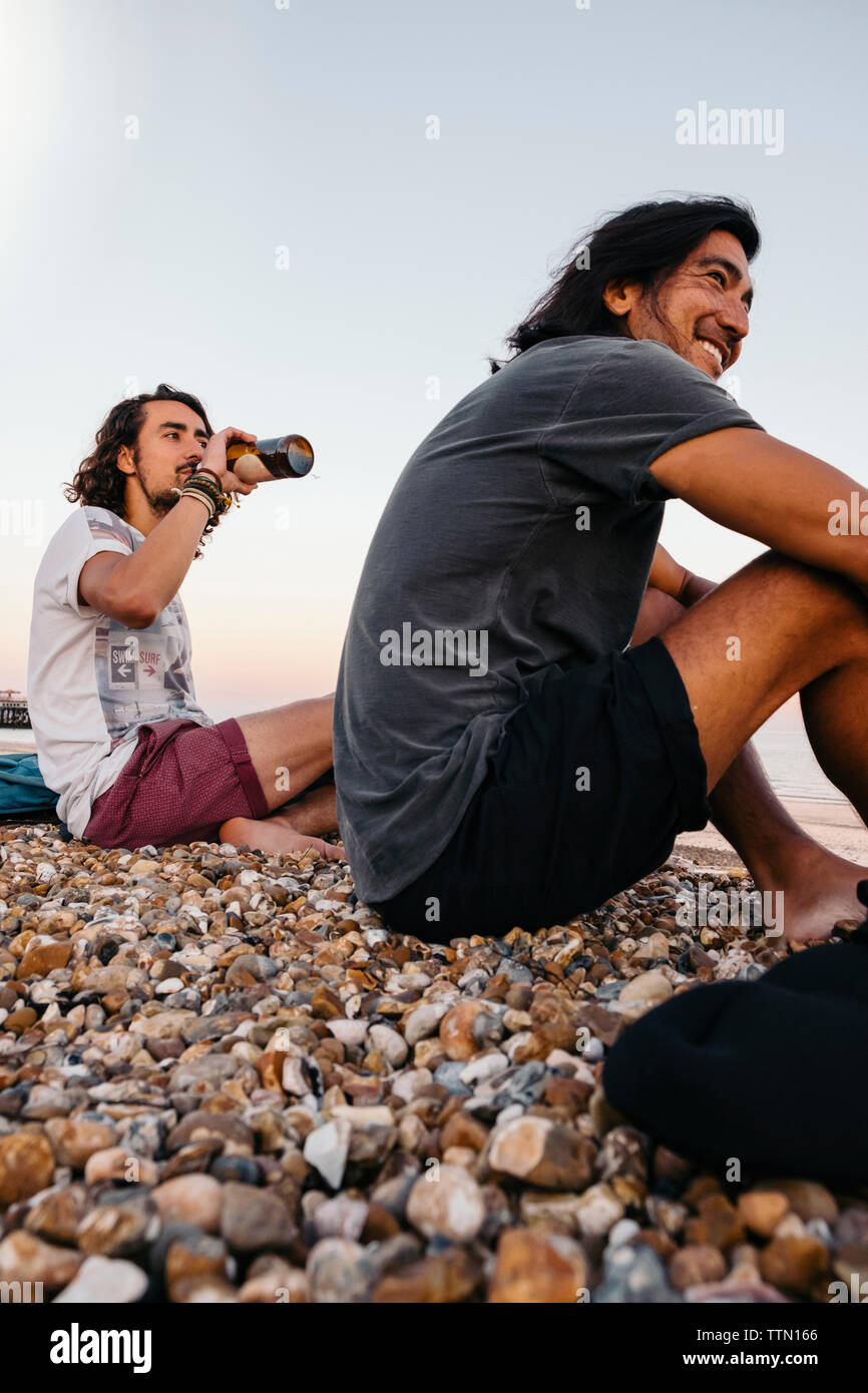 Seitenansicht der Freunde sitzen auf Kieselsteinen am Strand gegen Sky Stockfoto