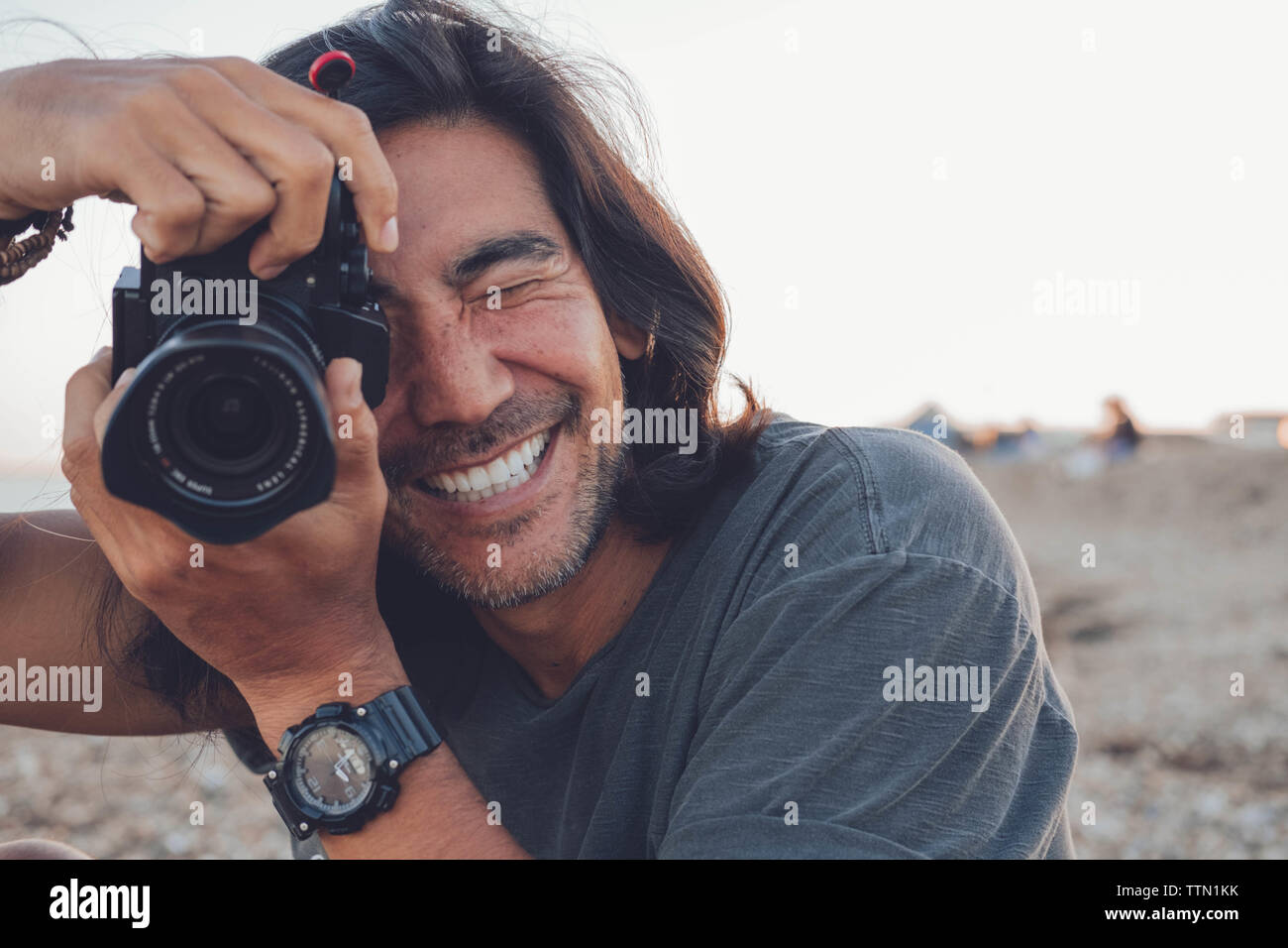 Person lächelnd in die Kamera am Strand, während Sie seine Kamera Stockfoto