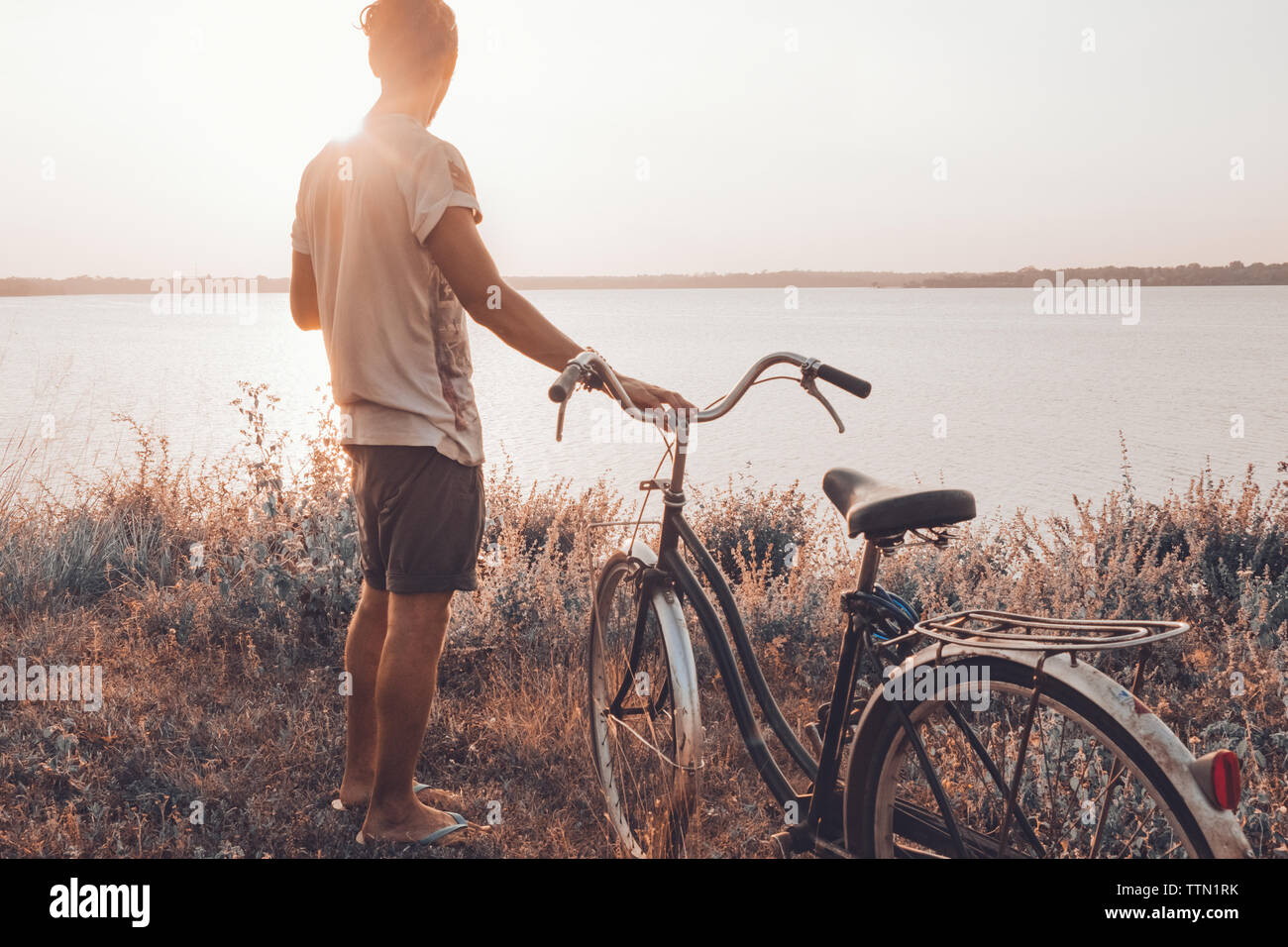 Mann neben seinem Fahrrad im Sommer im freien Blick auf den Sonnenuntergang Stockfoto