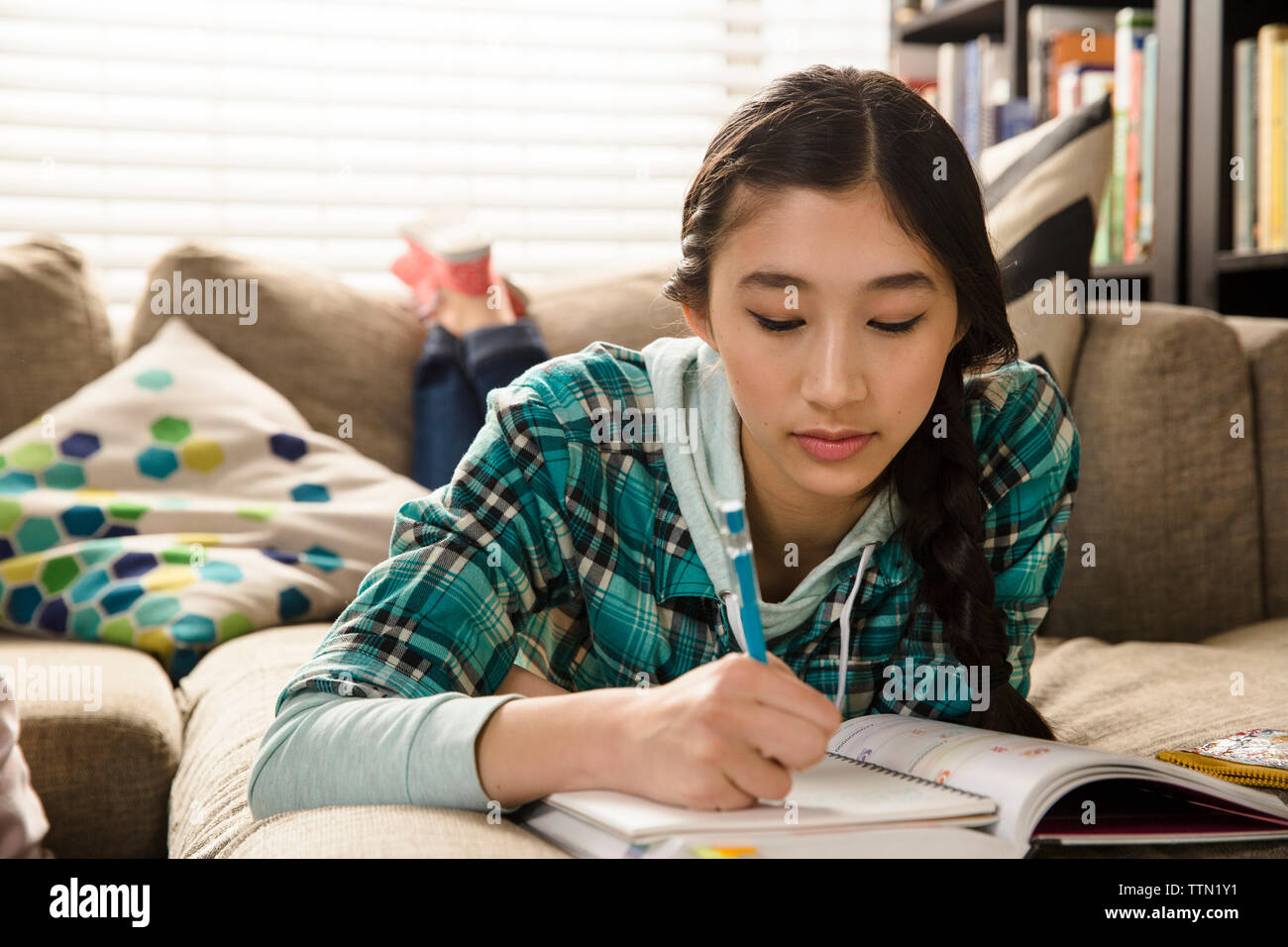 Junges Mädchen mit Hausaufgaben, während zu Hause auf der Couch liegend Stockfoto