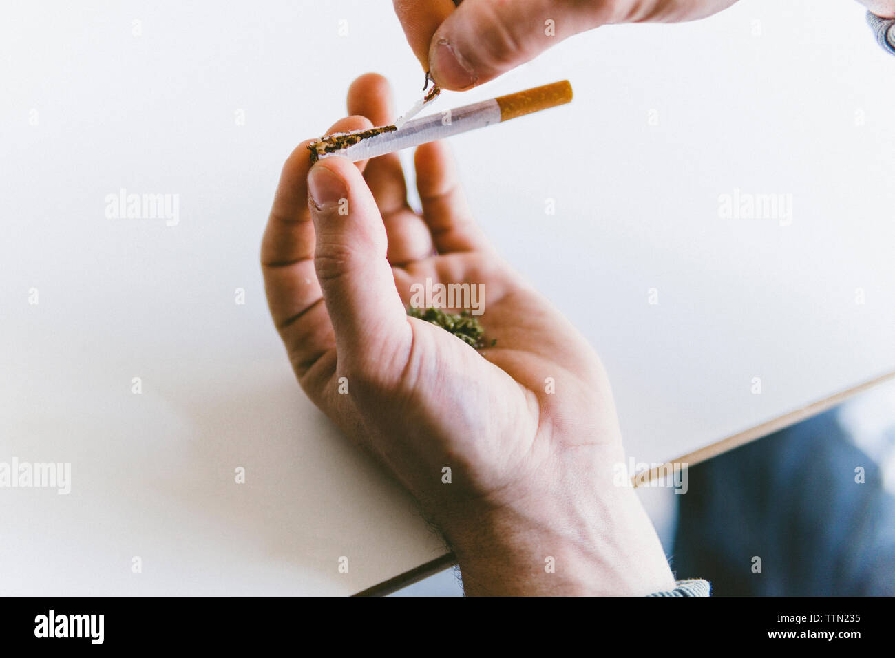 7/8 der Menschen Hand holding Marihuana Gelenke während Zigarette Reißen am Tisch Stockfoto