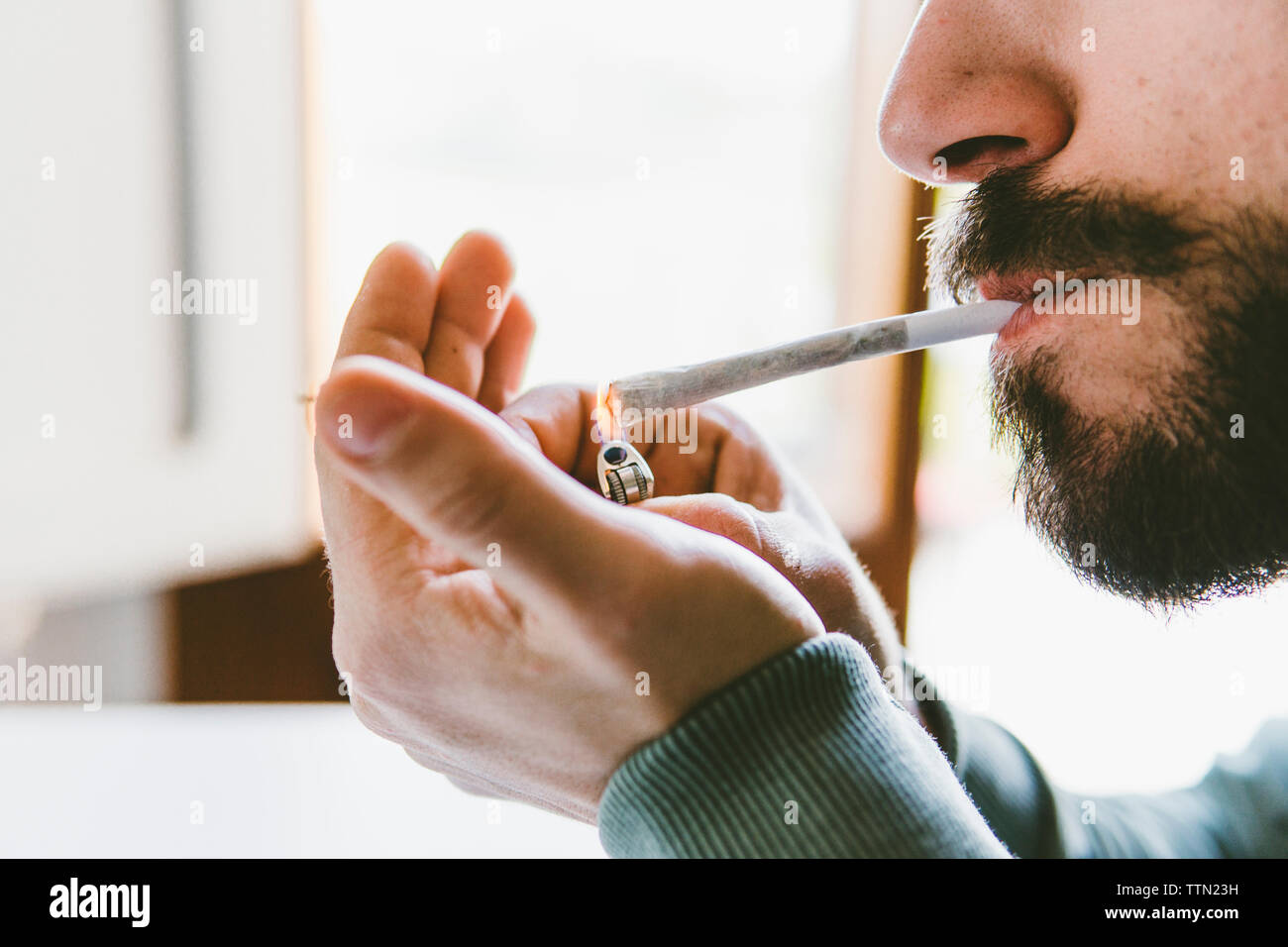 Mittelteil des bärtigen Mannes entzünden Marihuana gemeinsame mit Zigarettenanzünder zu Hause Stockfoto