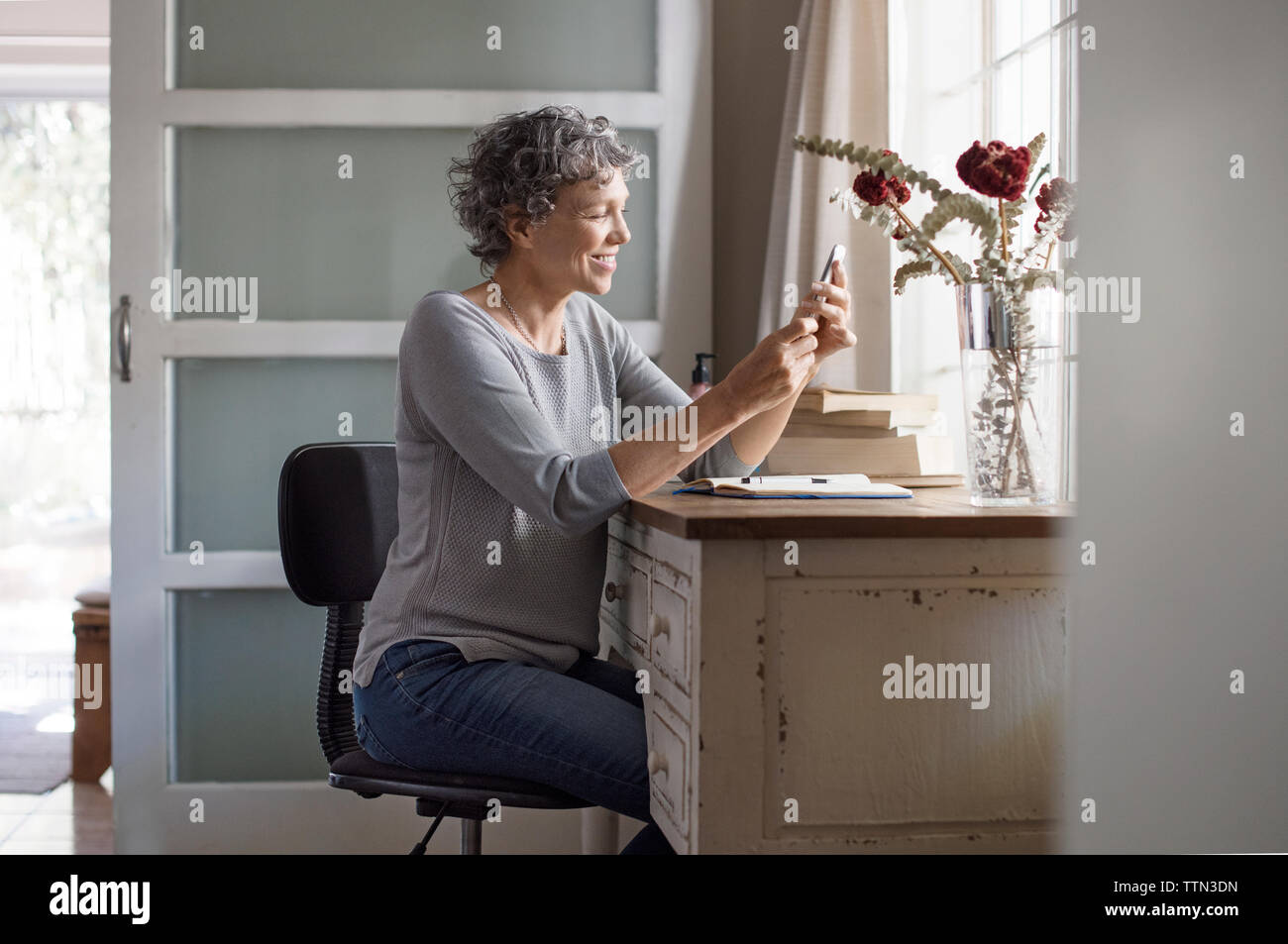 Reife Frauen an smart phone suchen und zu Hause lächeln Stockfoto