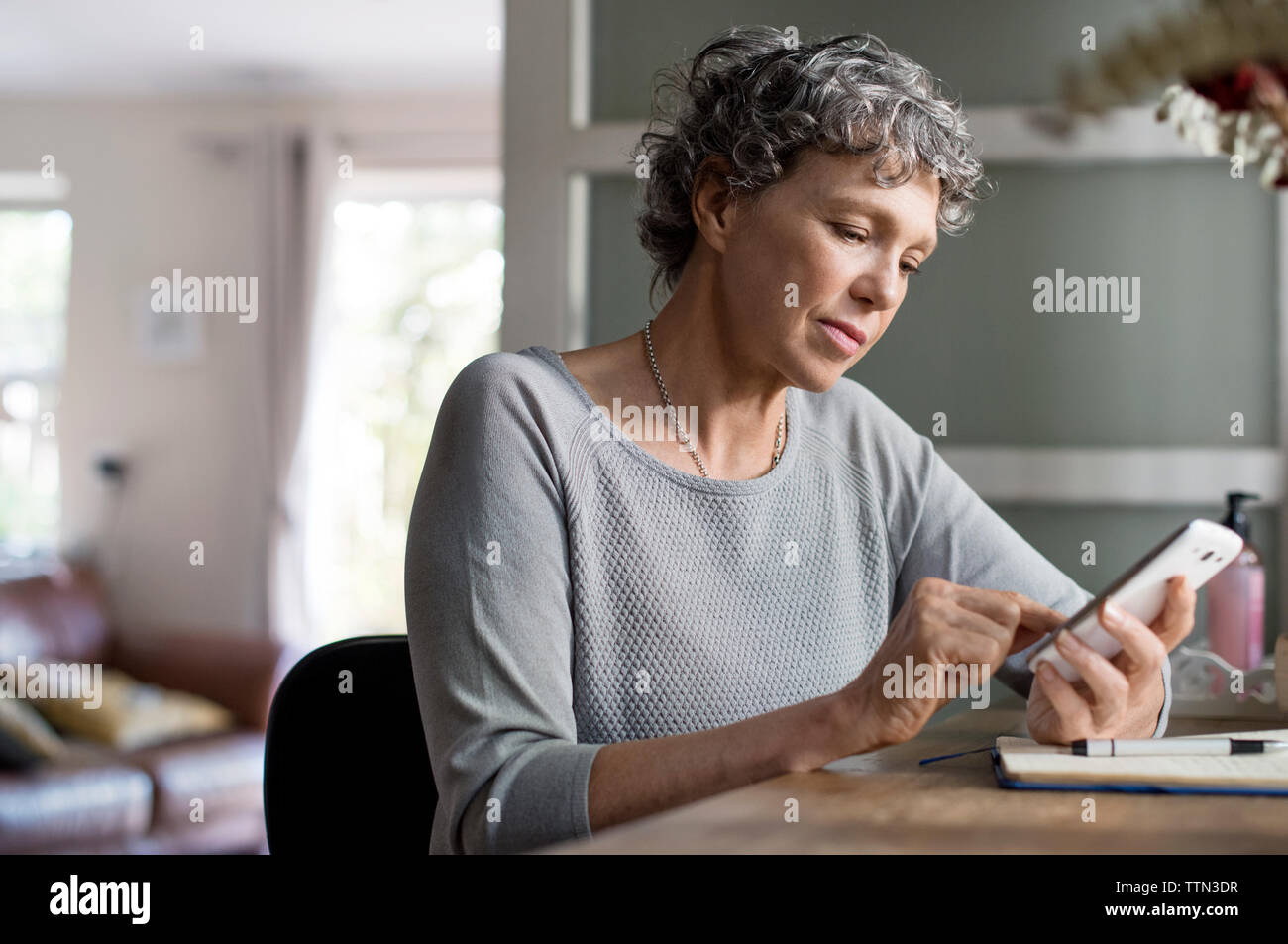Reife Frau mit Smart Phone, während zu Hause arbeiten Stockfoto